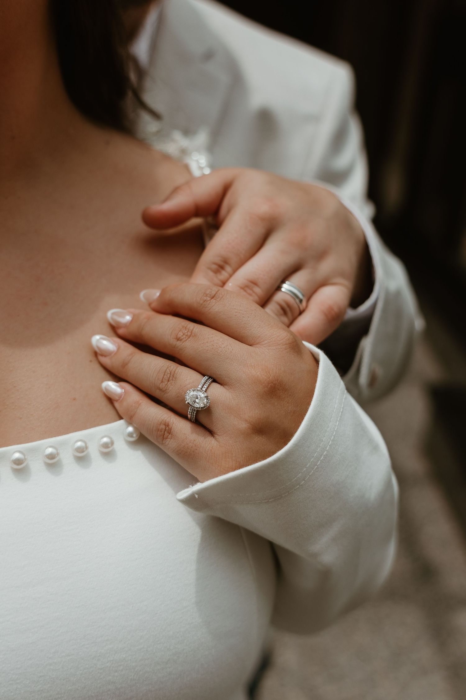 Elegant engagement ring detail shot with pearl buttons on white formal attire.