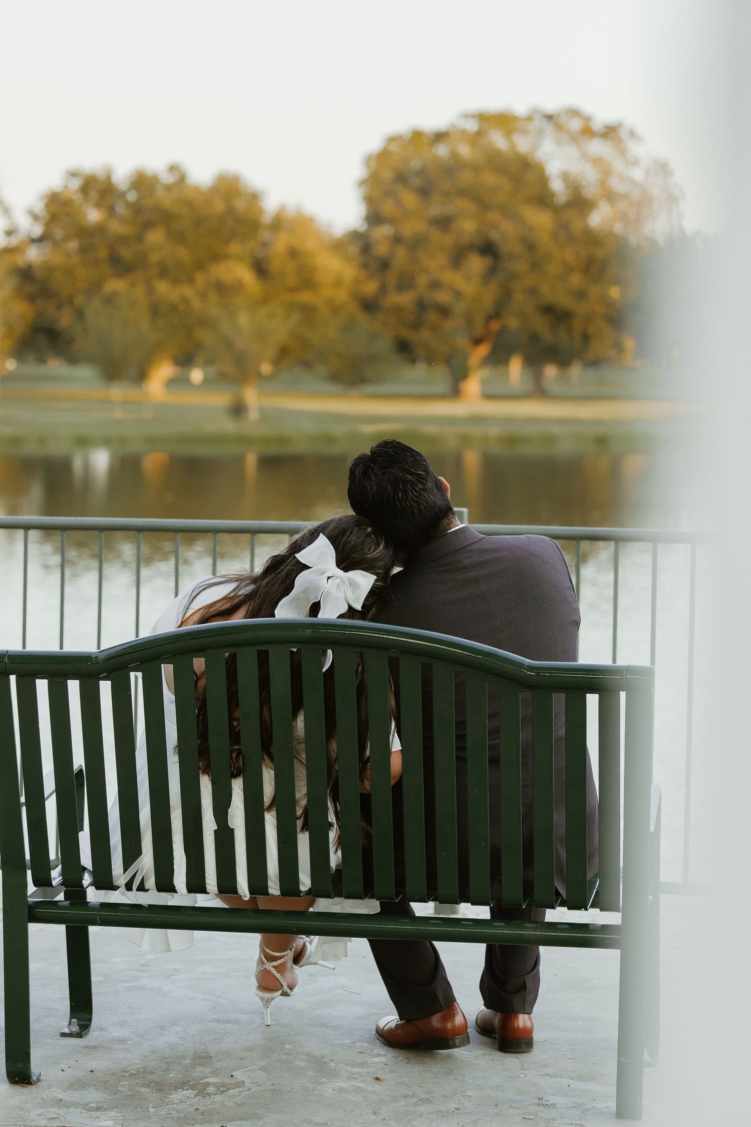 Couple sits together on green park bench overlooking peaceful lake and autumn trees.