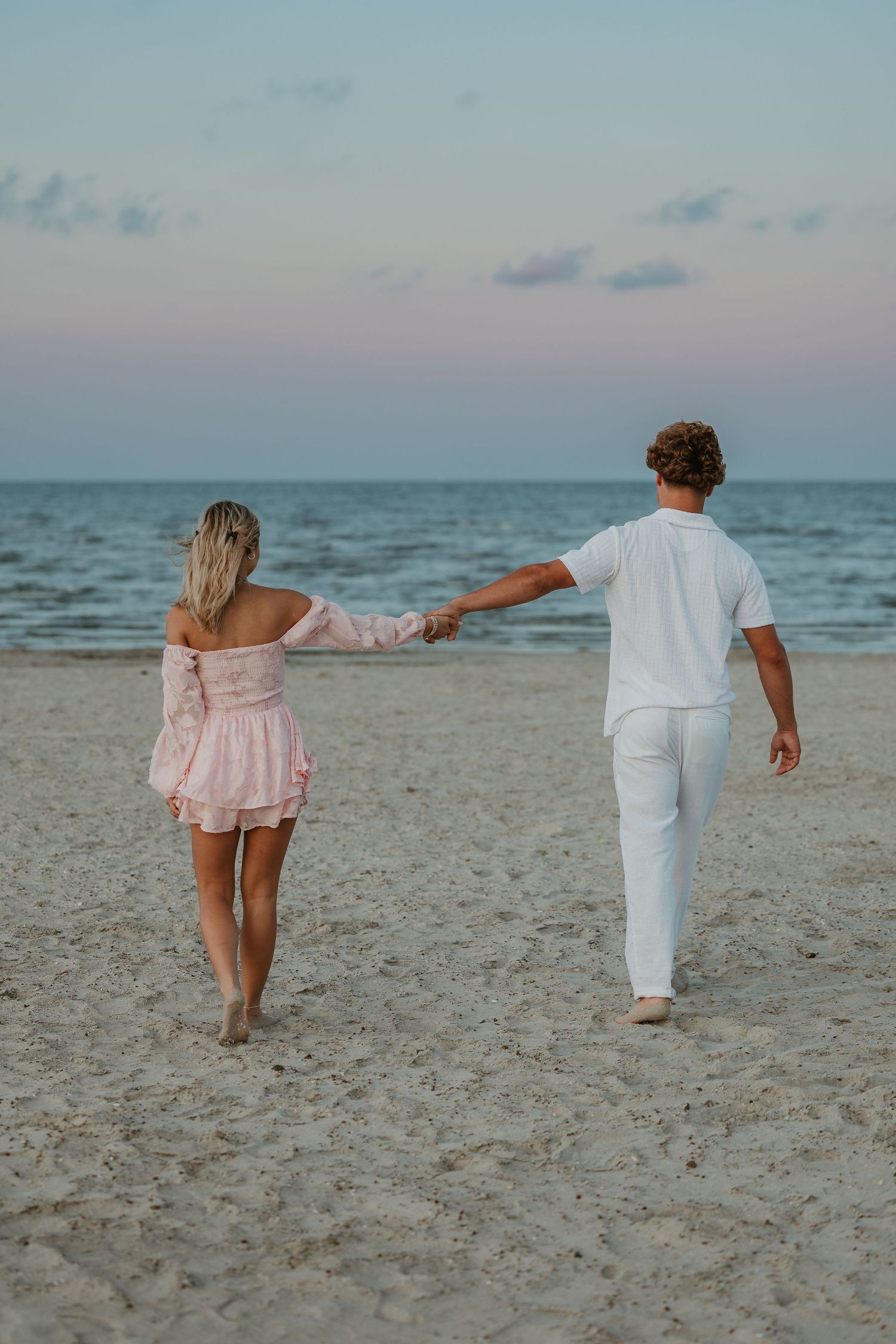 A couple strolling together on a beach with the ocean in the background at dusk.