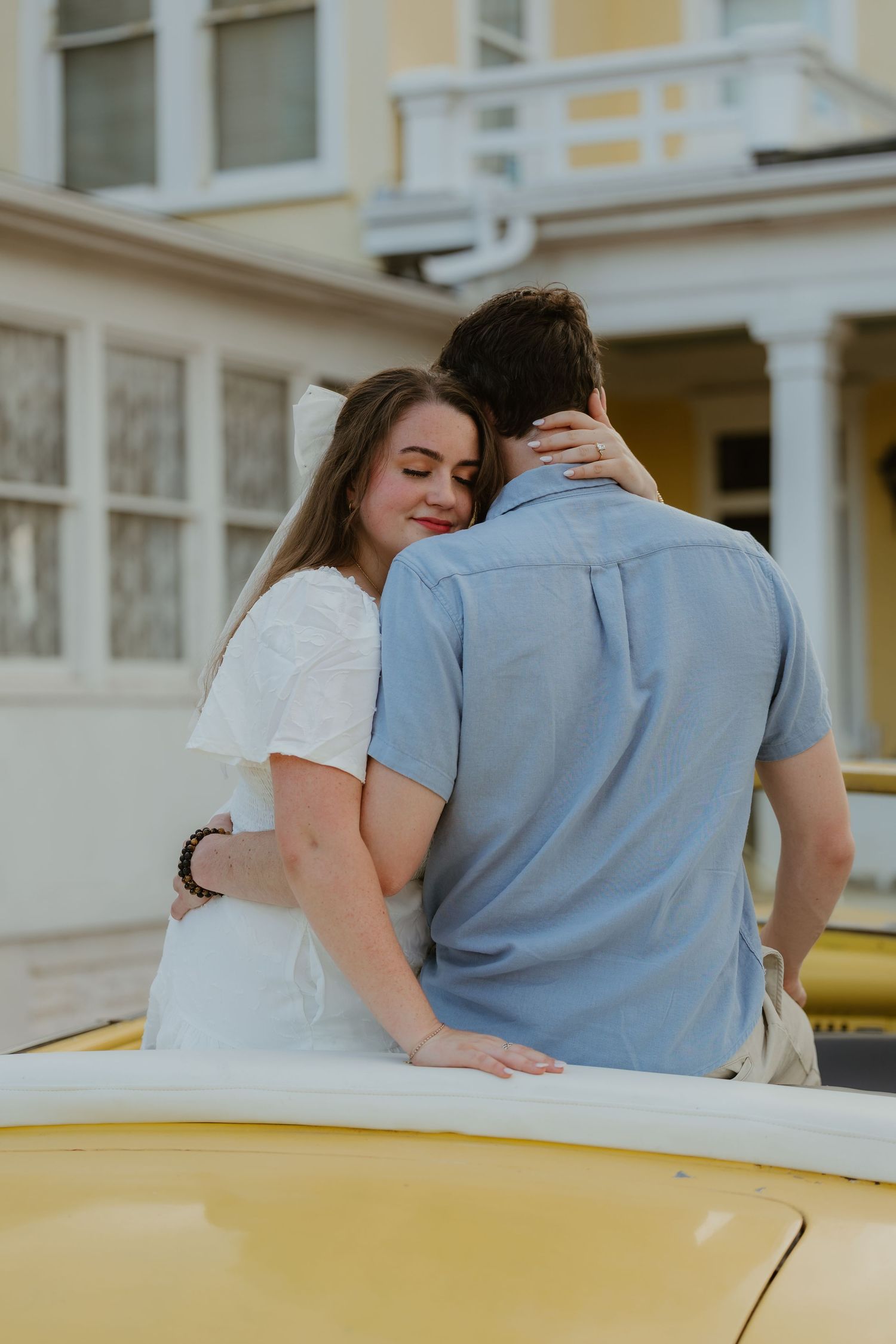A romantic couple shares a moment on a vintage yellow car.