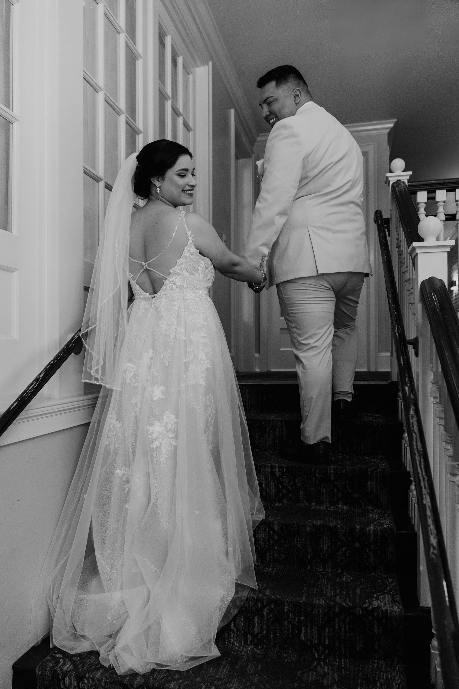 Wedding couple navigating stairs together in elegant white attire.