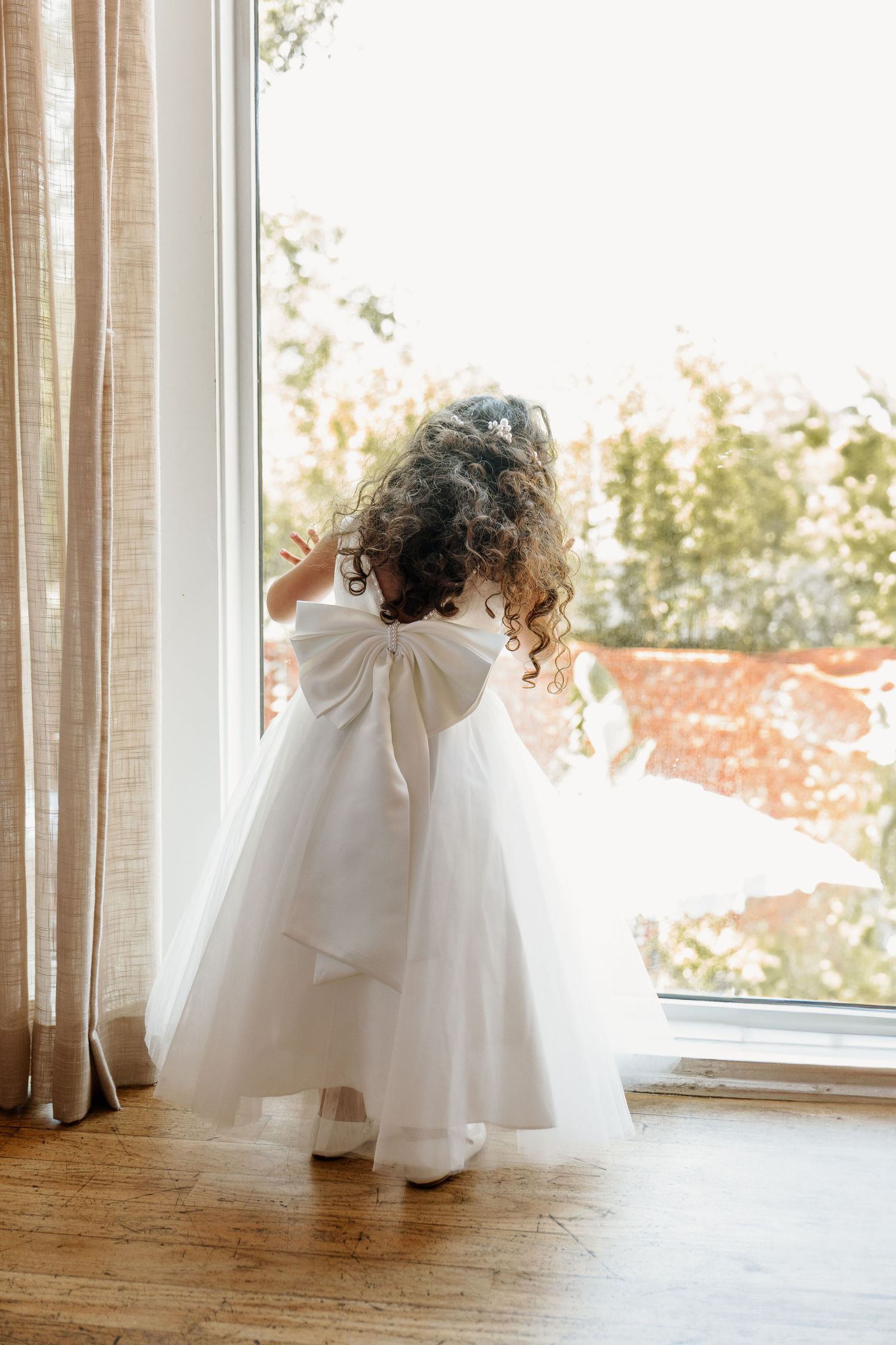 A small figure in a white dress twirls by a sunlit window.