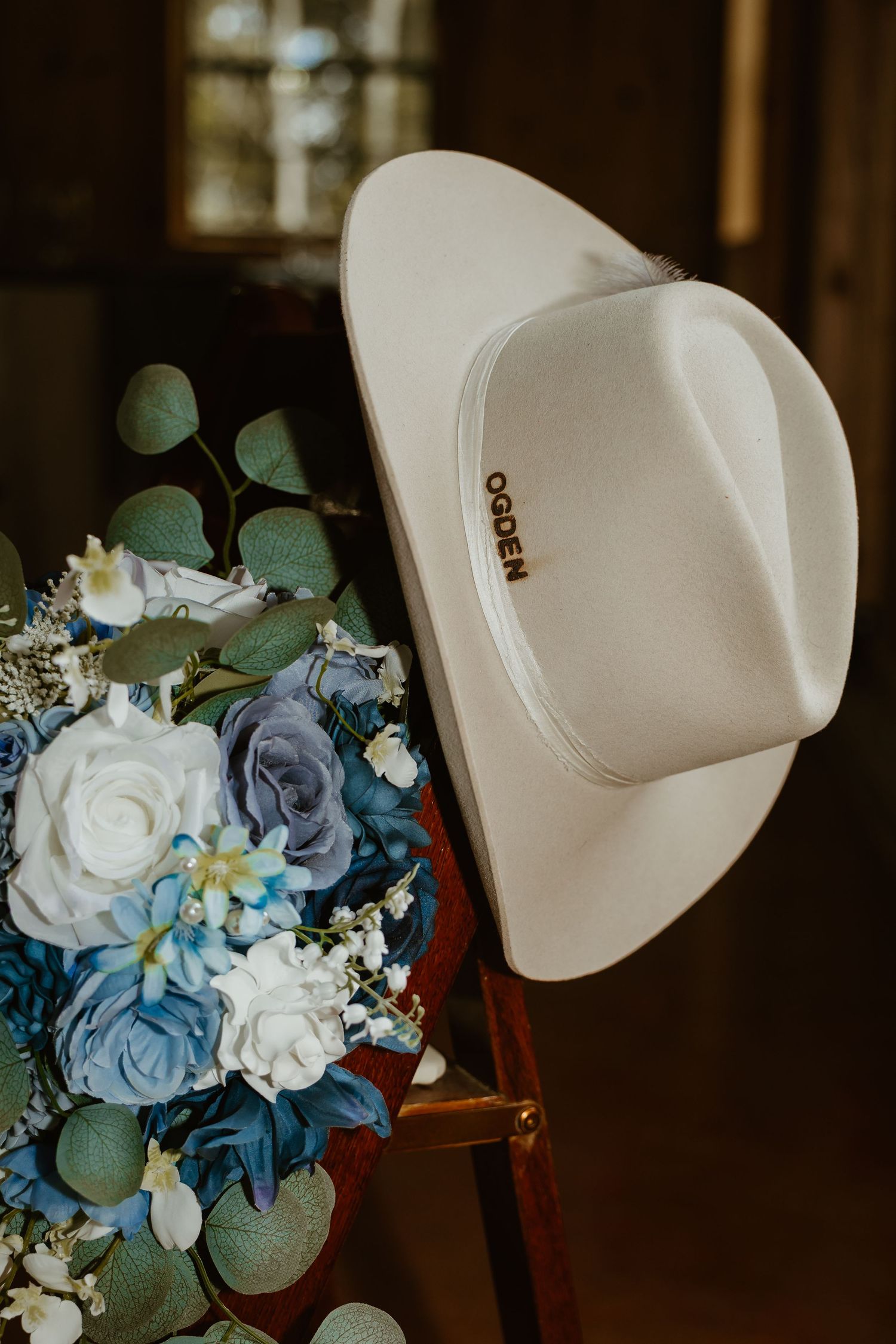 White cowboy hat adorned with a blue and white floral arrangement for a country wedding.