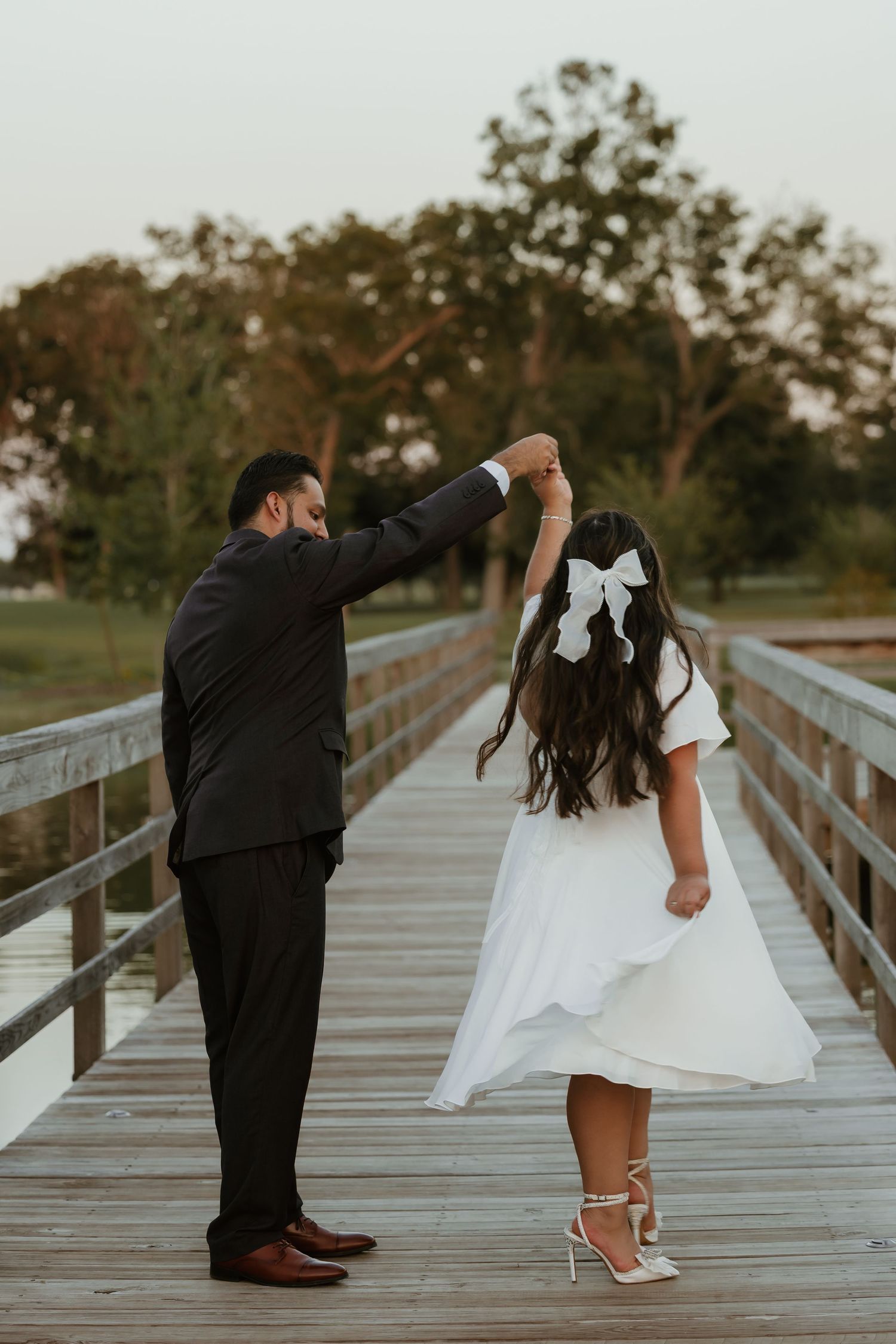 Couple dancing on wooden boardwalk during sunset, white dress twirling.