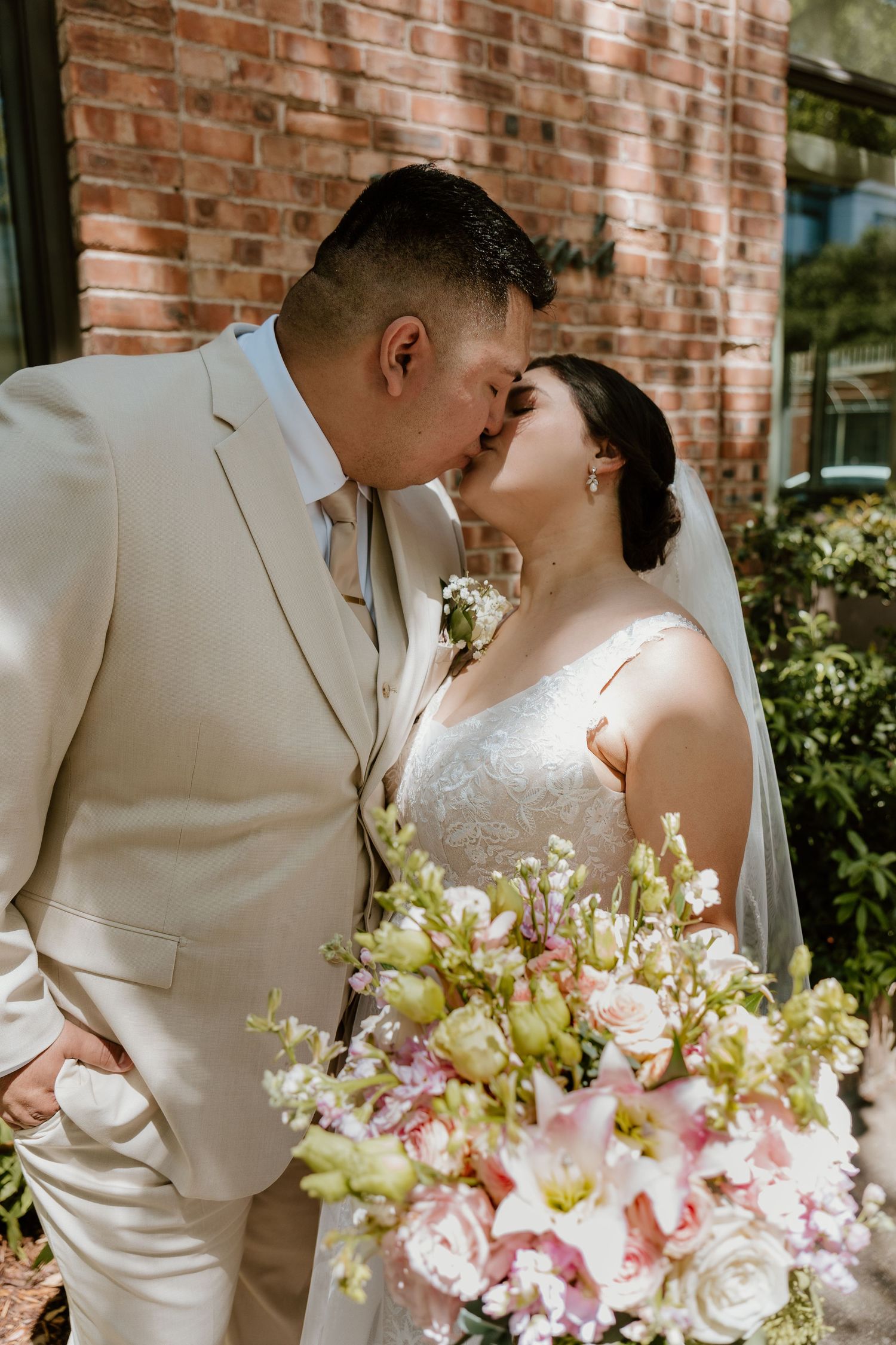 Intimate wedding portraits with pink and white floral bouquet against brick backdrop.