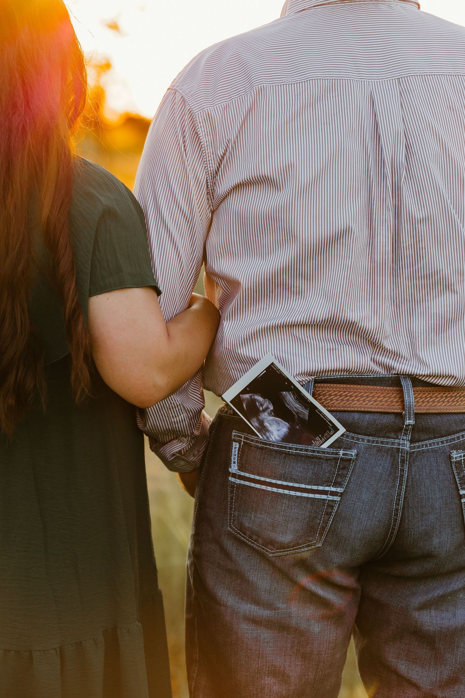 A close-up shot of a couple holding ultrasound photos in their back pocket at sunset.