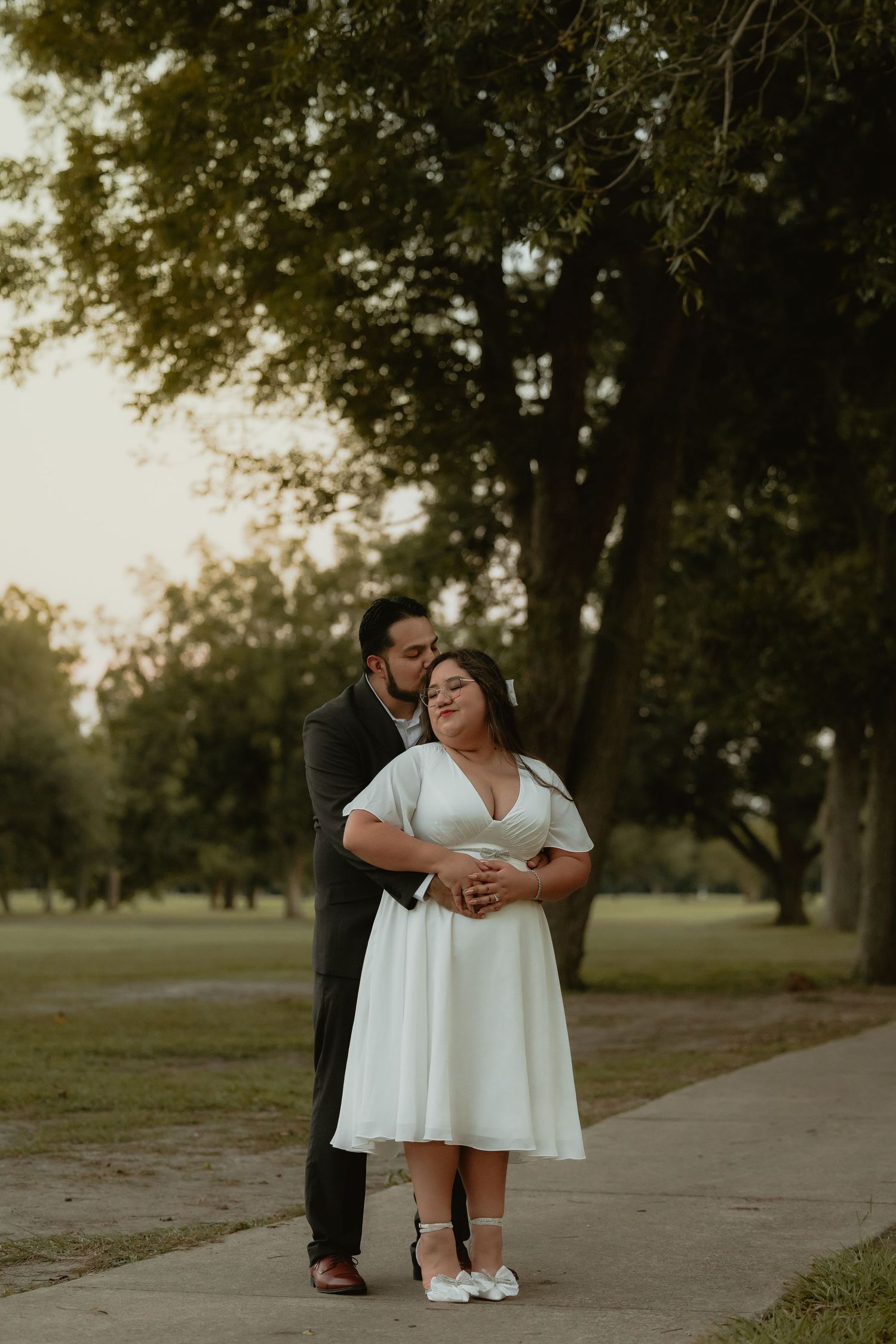 Romantic couple embrace on path during golden hour with trees in background.