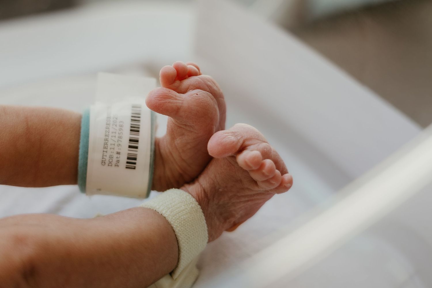 Close-up of newborn baby feet with hospital identification bracelet in a white bassinet.