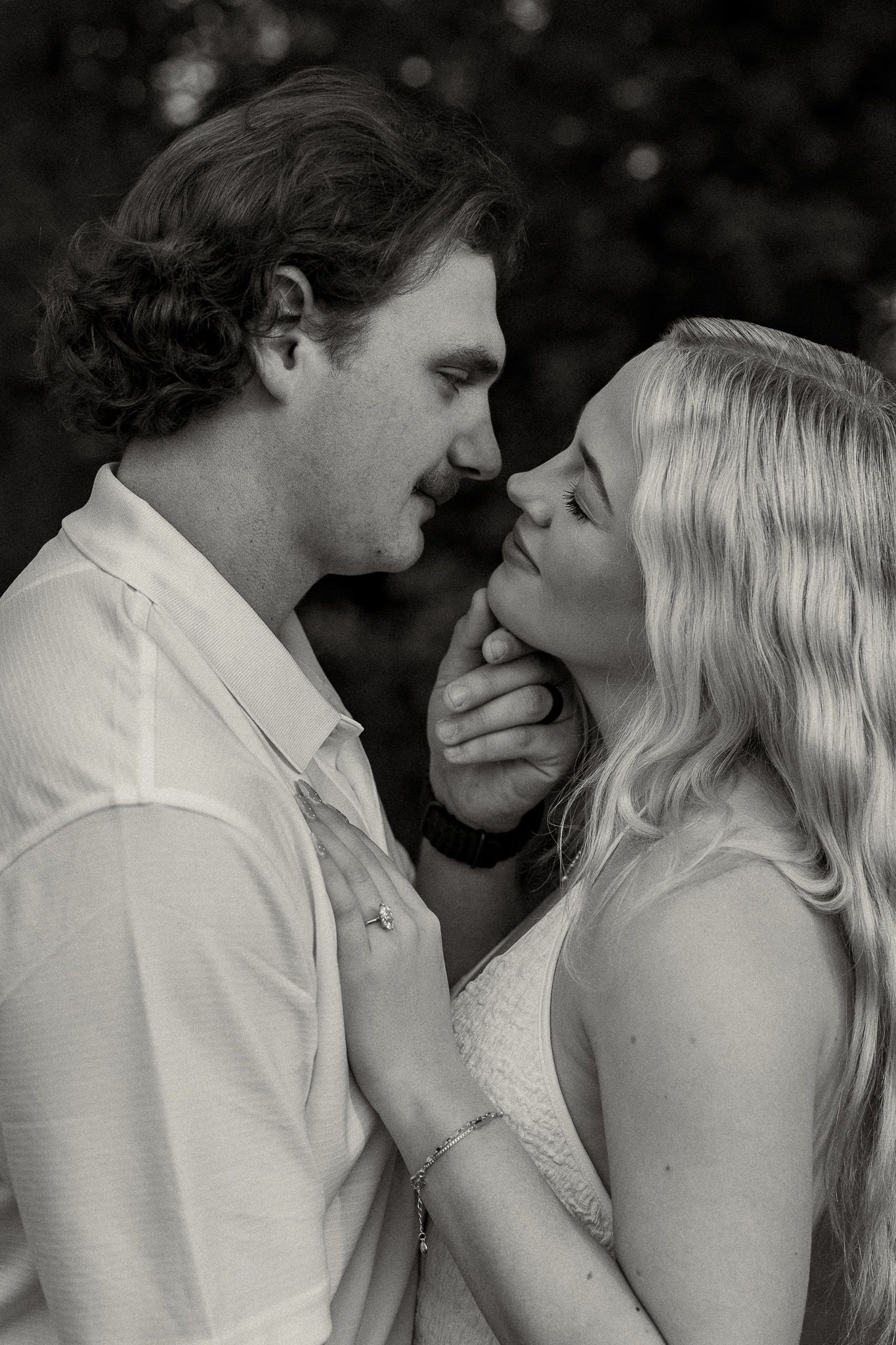 Black and white photo of a romantic couple sharing an intimate moment, about to kiss outdoors.