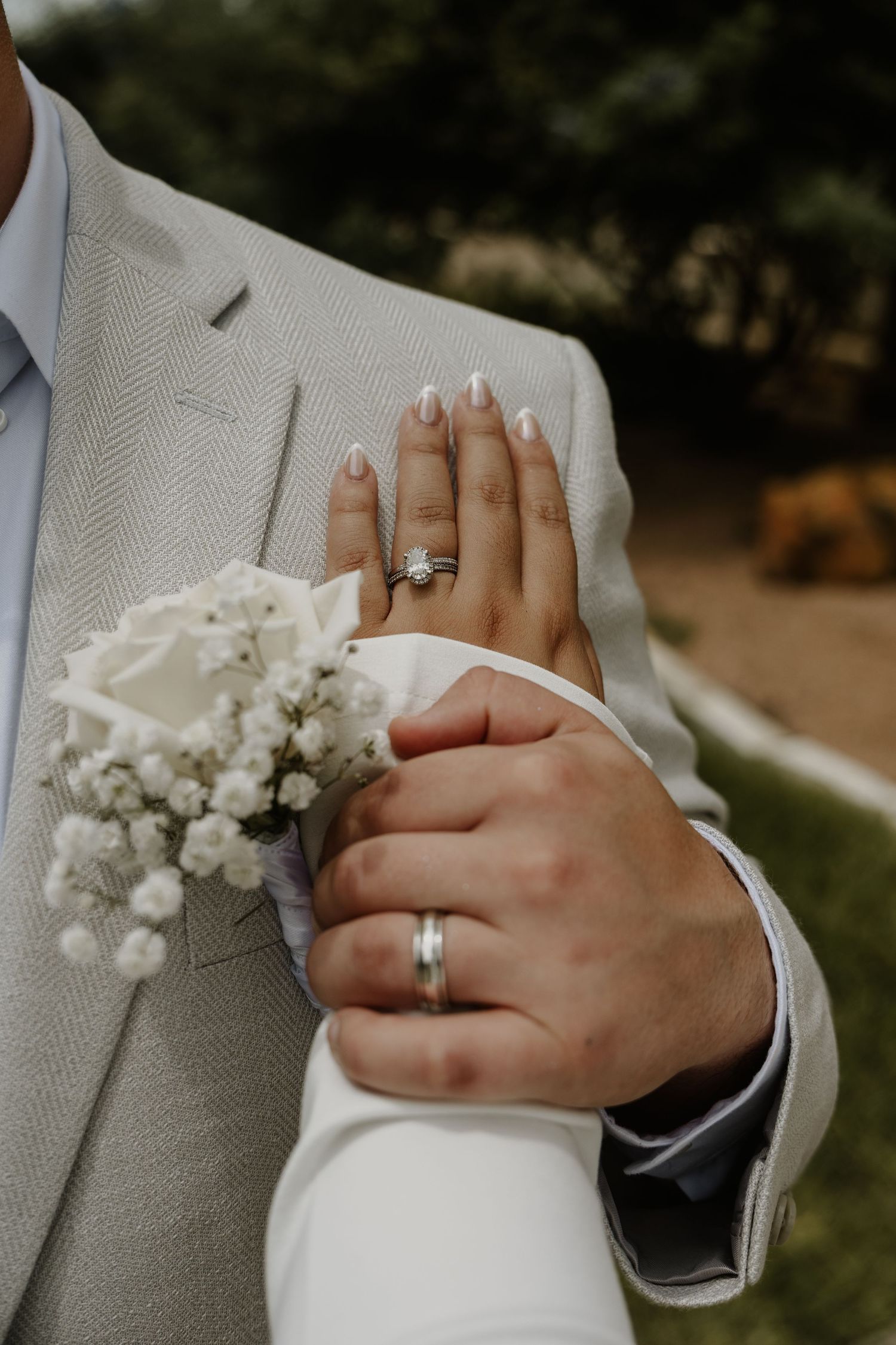 Close-up of wedding rings and a delicate white floral boutonniere against a light gray suit.