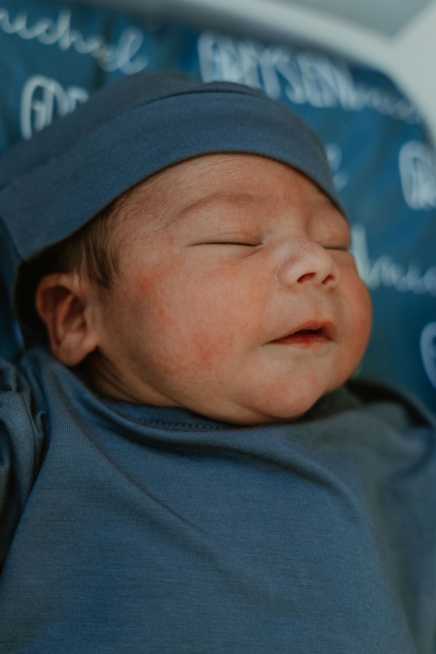 Newborn baby wearing blue cap sleeping peacefully.