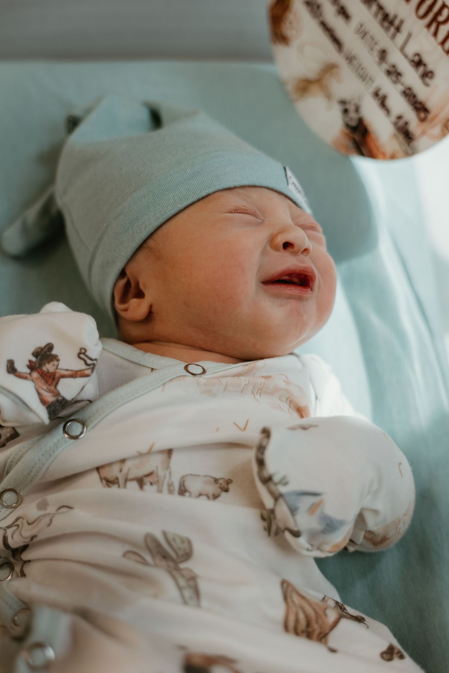 Newborn baby wearing printed onesie resting in hospital bassinet.
