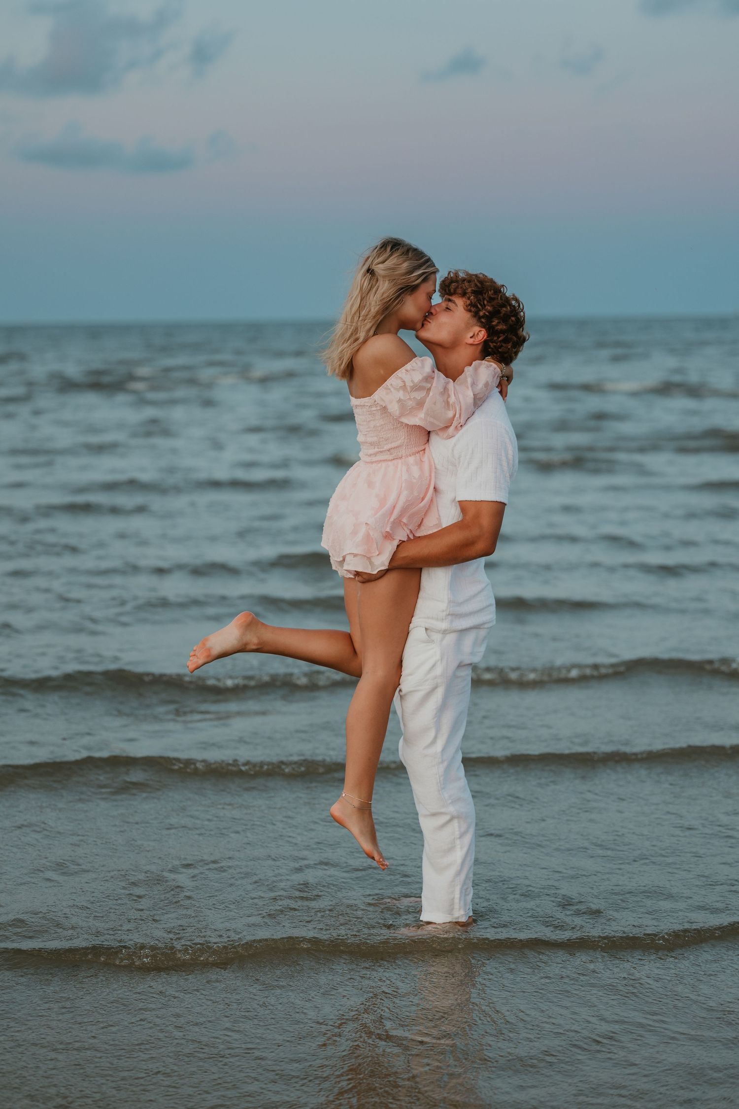 A couple embracing and sharing a romantic moment in the ocean waves at sunset.