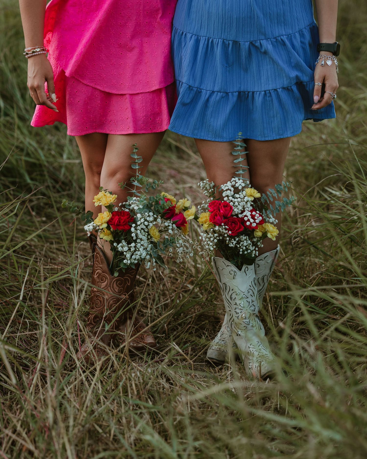 Close-up of pink and blue dresses with decorated boots in tall grass.