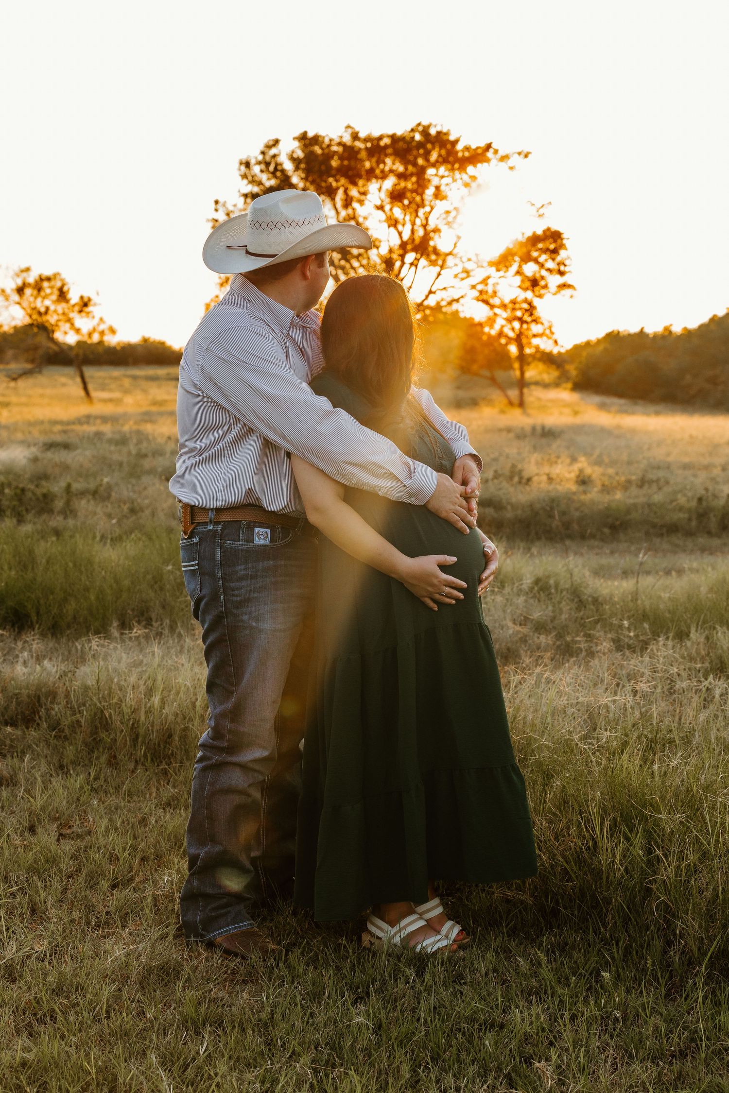 A couple embraces in a golden field during their maternity photo session.