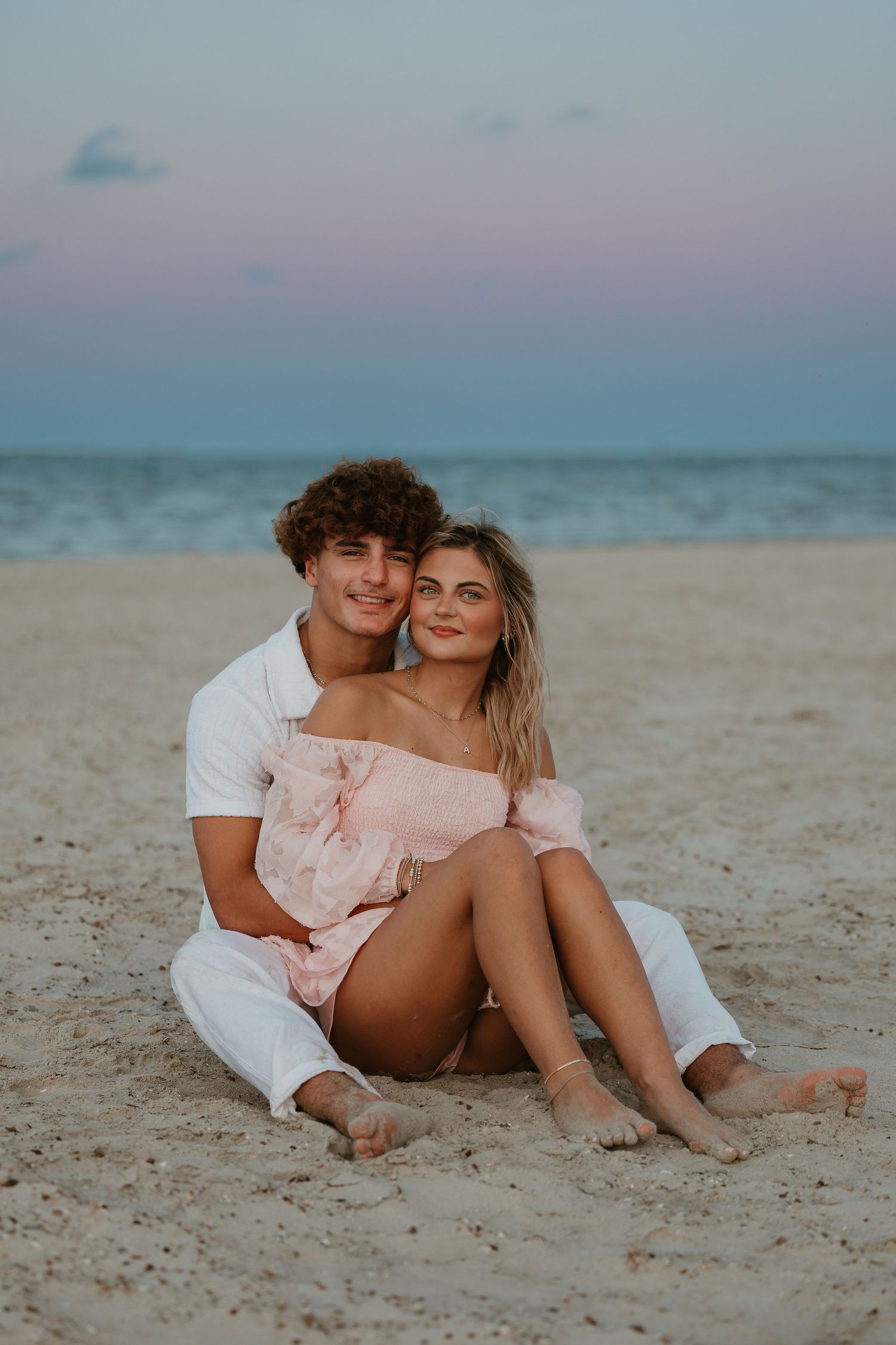 A romantic couple sitting together on the beach sand at twilight.
