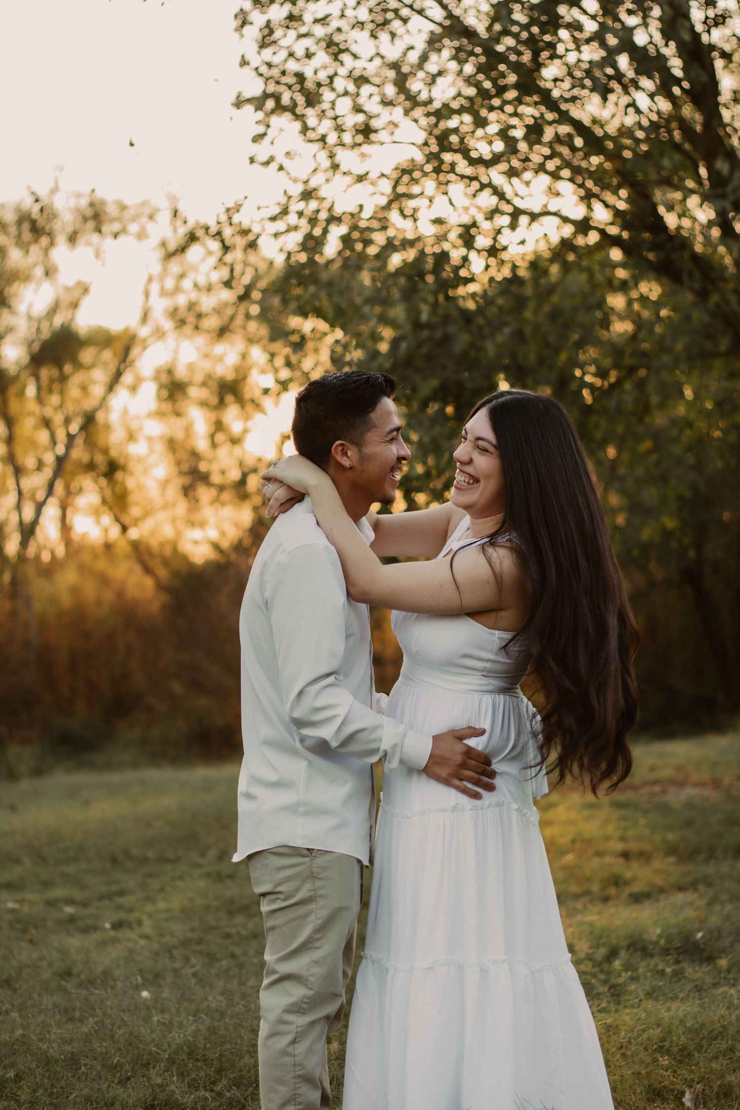 A couple shares a joyful embrace in a field during golden hour.