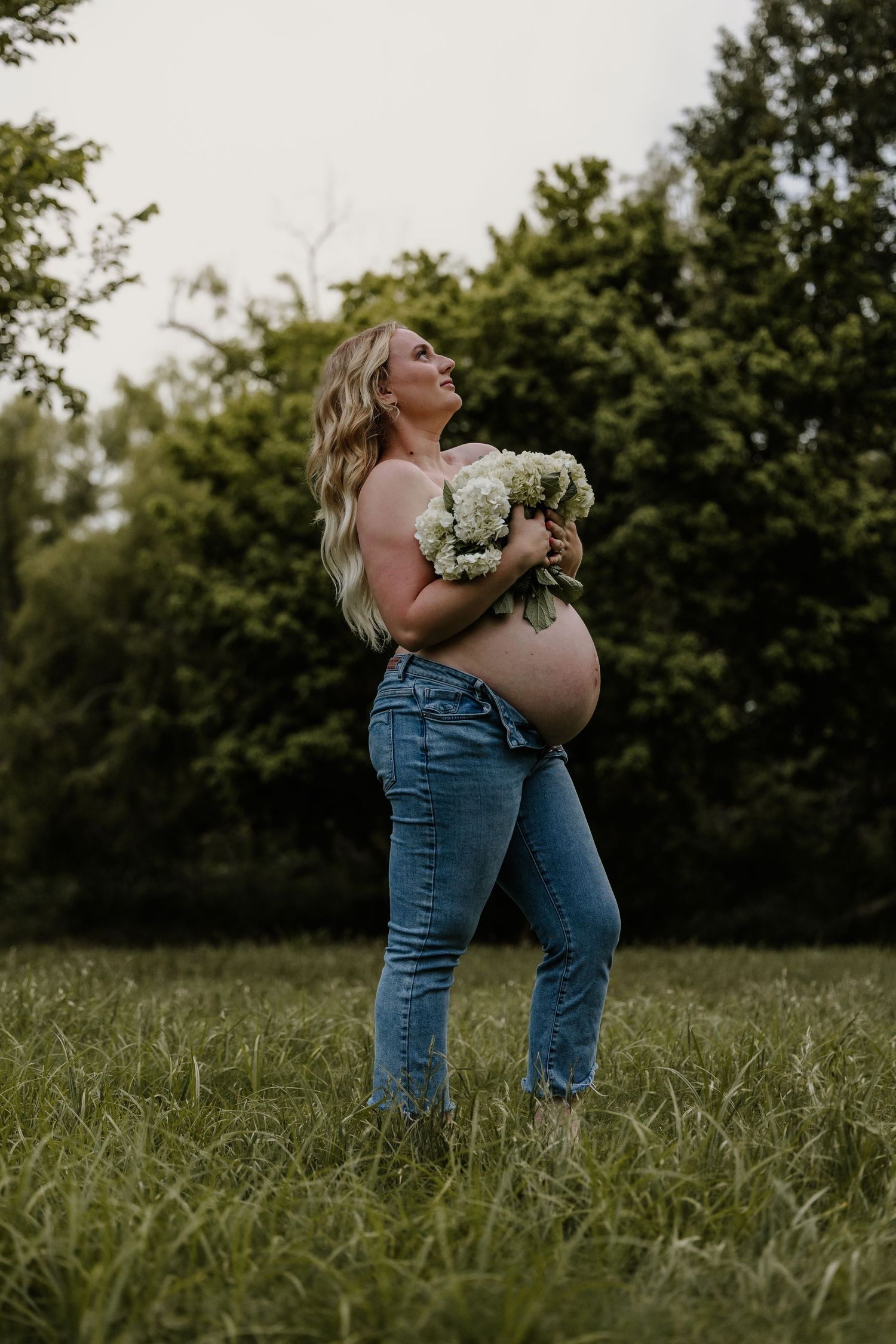 An artistic maternity portrait in jeans holding white flowers as a top.