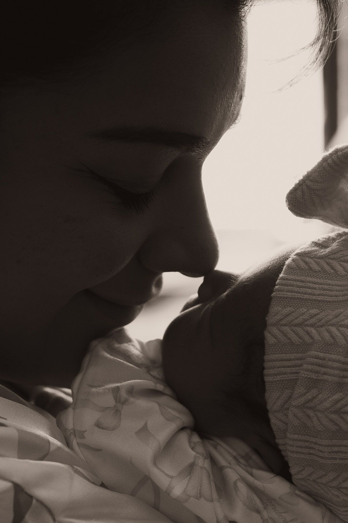 Black and white photo of a mother tenderly holding and gazing at her newborn baby in a serene, intimate moment.