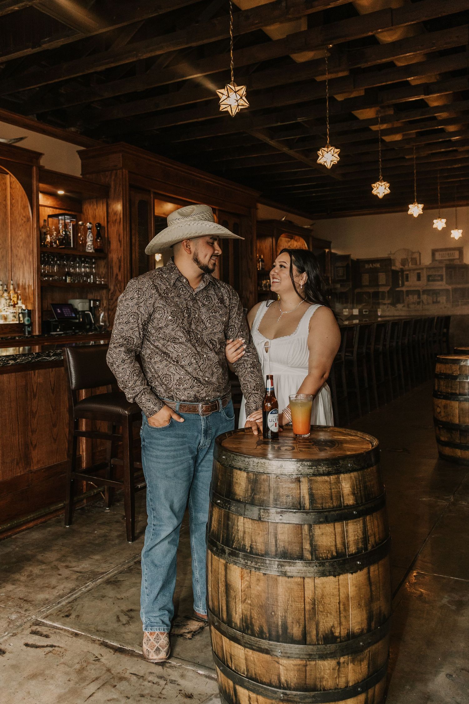 A couple shares drinks at a rustic bar with wooden barrels and exposed ceiling beams.