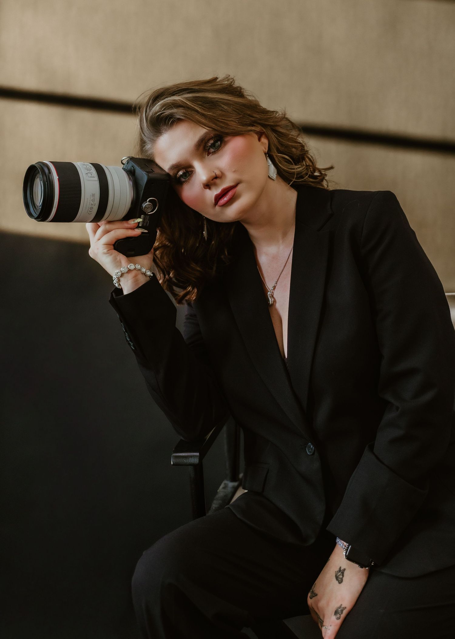 A photographer in black attire poses with professional camera equipment against a neutral background.
