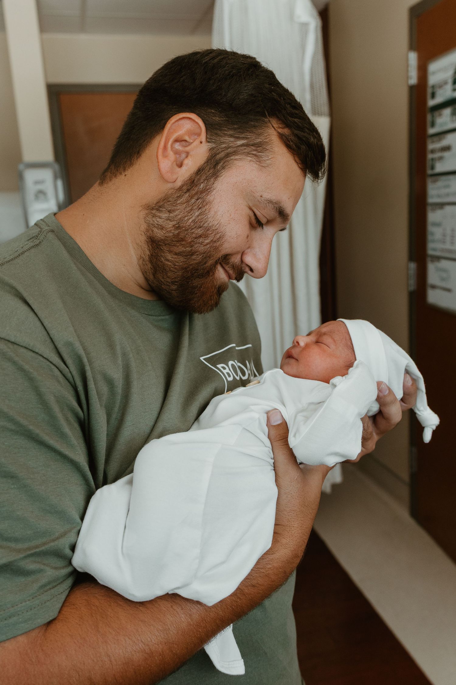 A tender moment between first time dad and newborn baby wrapped in white blanket.