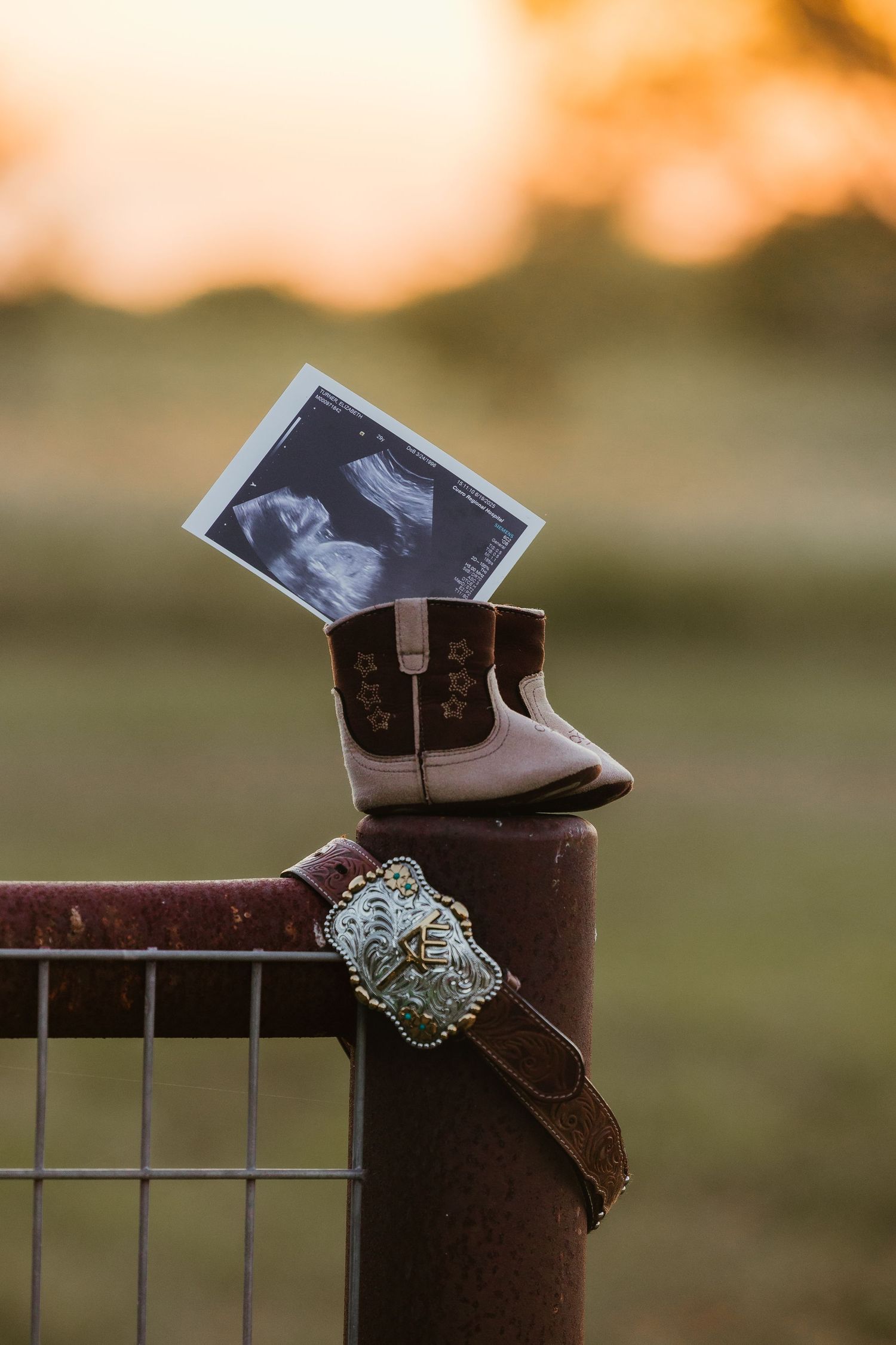 Baby boots and ultrasound photo displayed on rustic fence post.