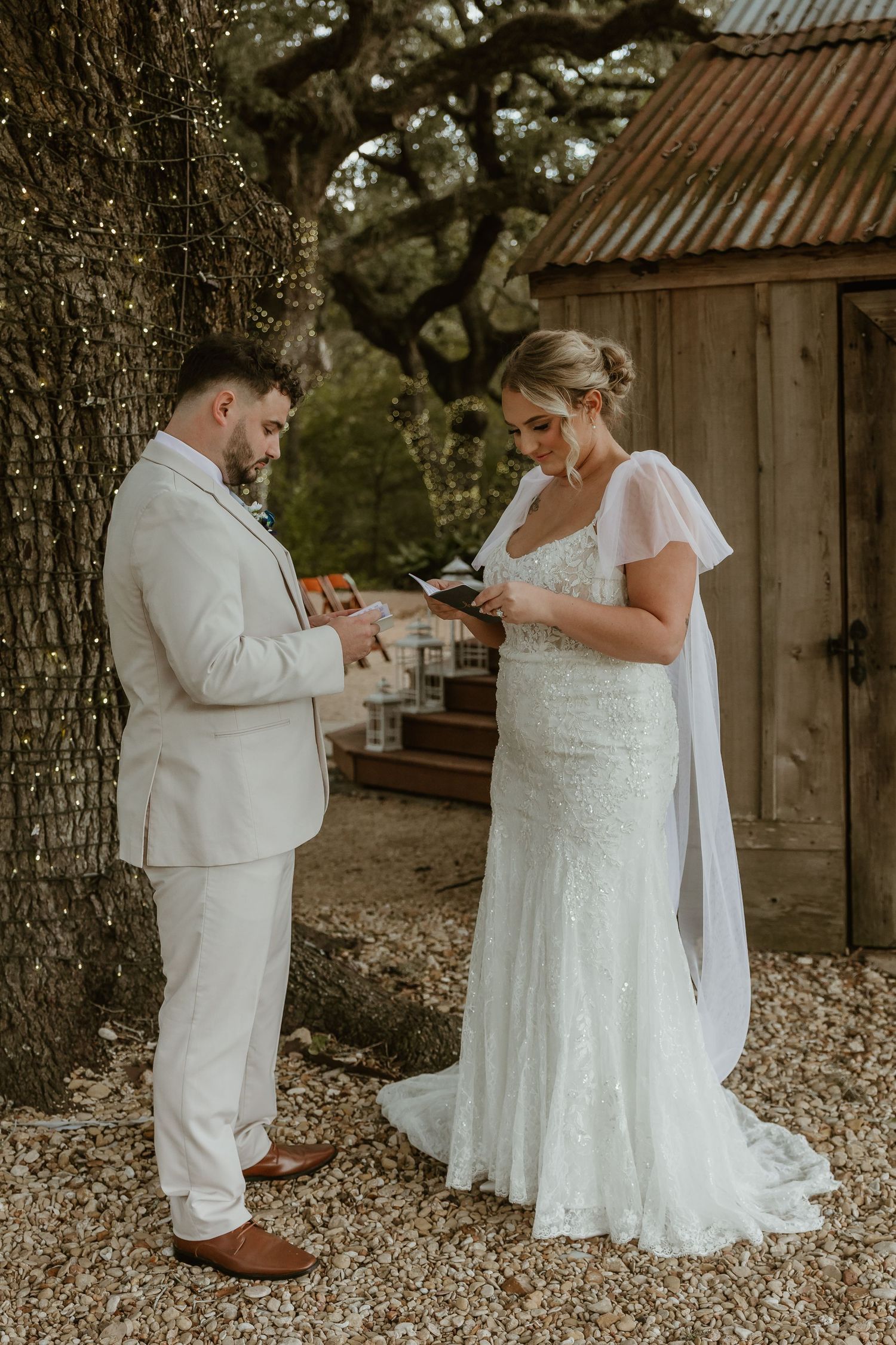 Wedding couple in white attire poses for photos outside a rustic wooden barn.