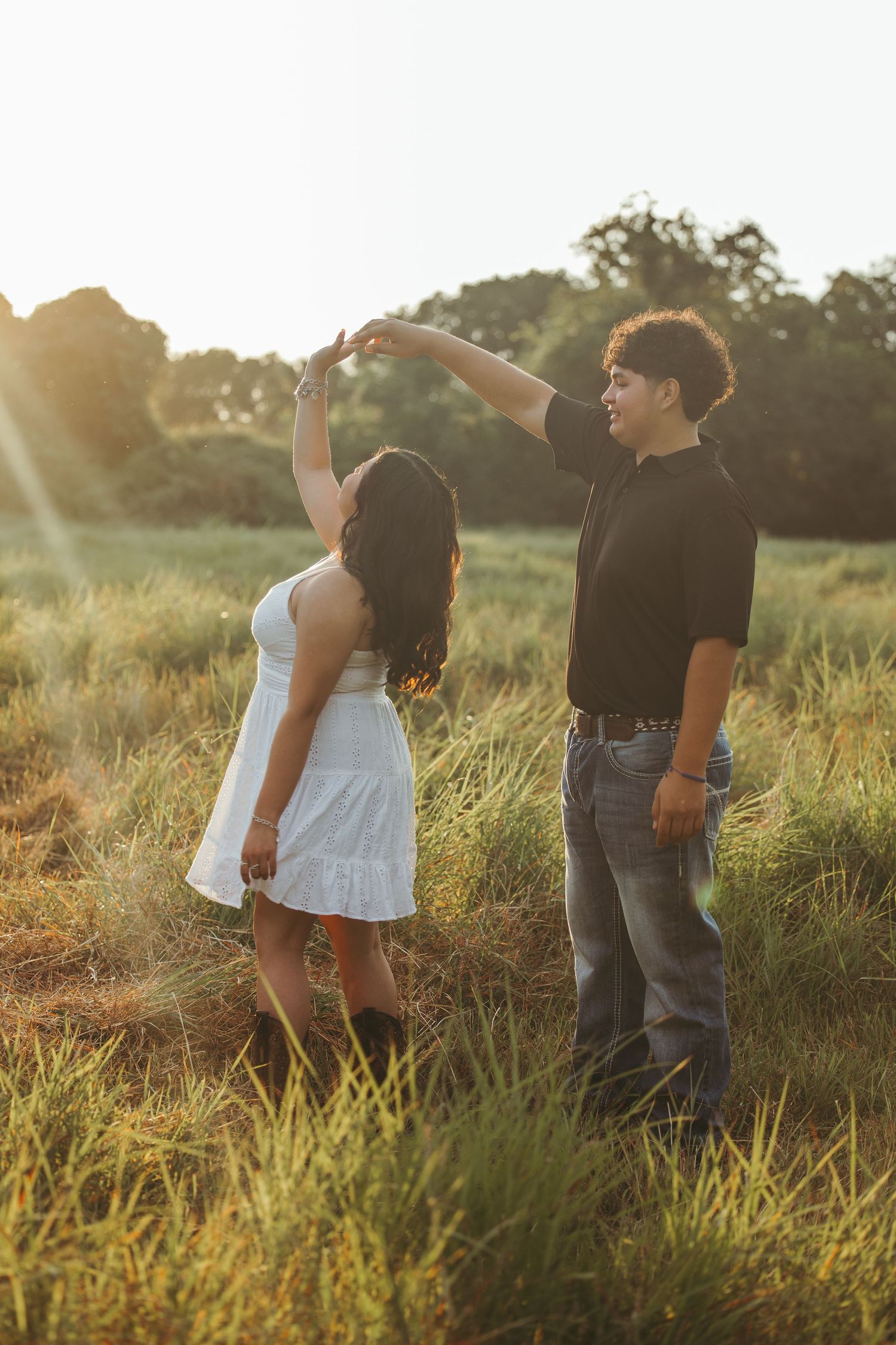 Couple dances playfully in golden hour light among tall grass.