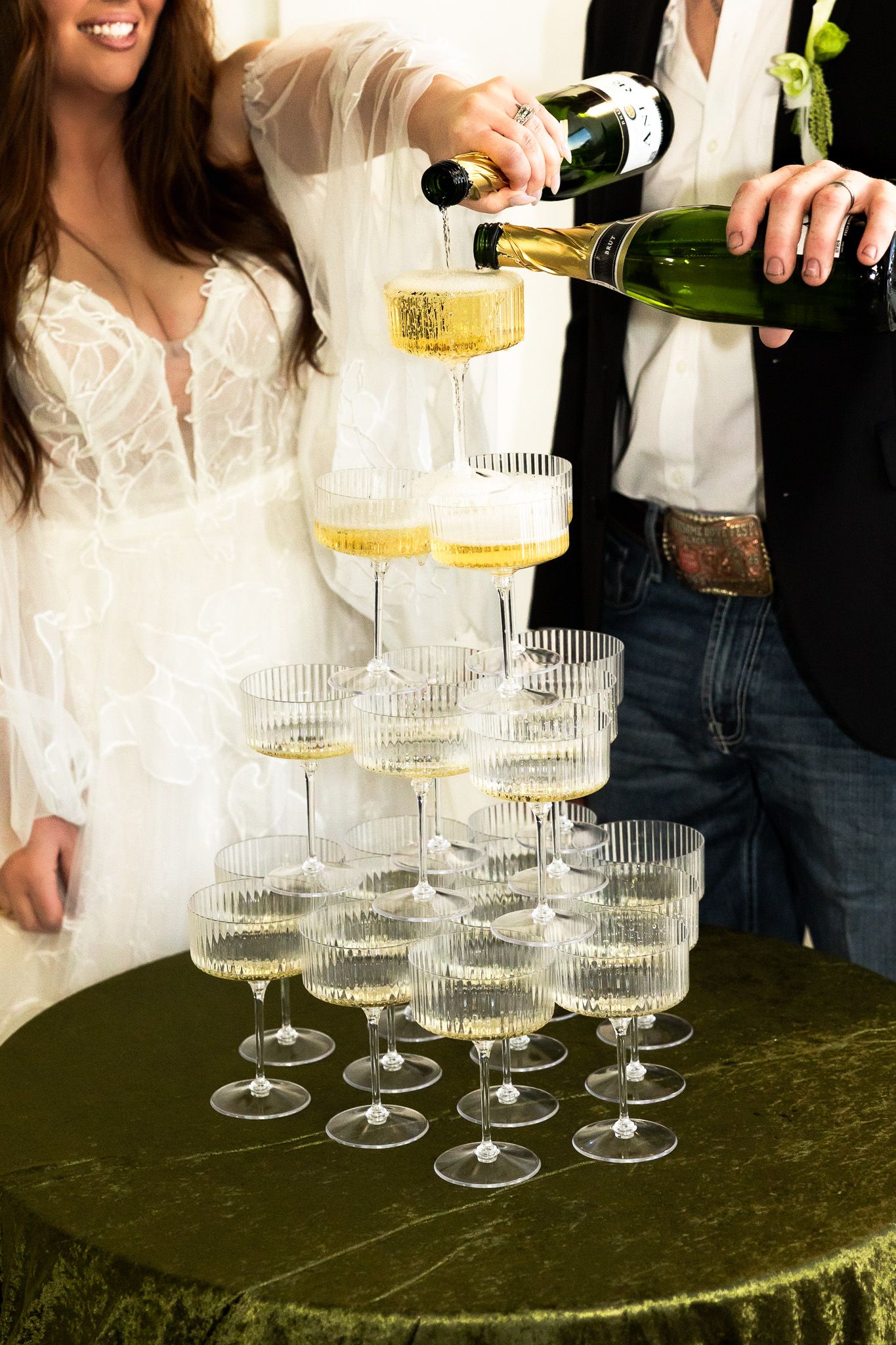 Bride and groom pouring champagne into a elegant tiered tower of crystal coupe glasses at their wedding reception.