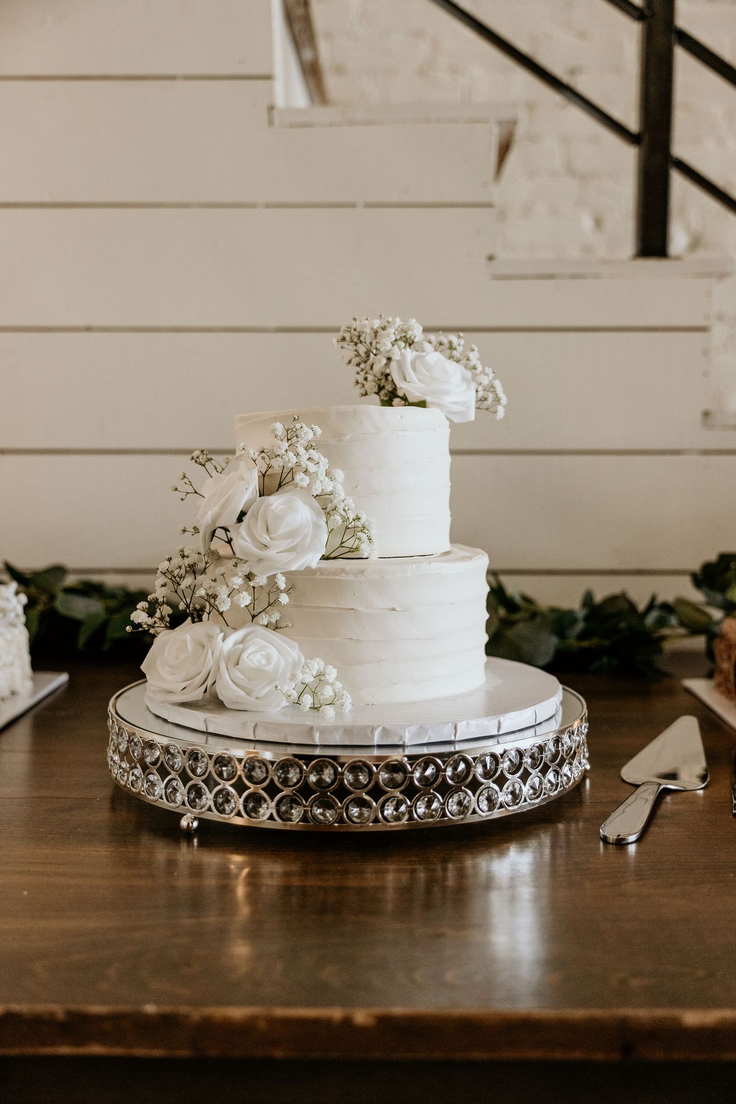 Three-tiered white wedding cake with floral decorations on an ornate silver cake stand.