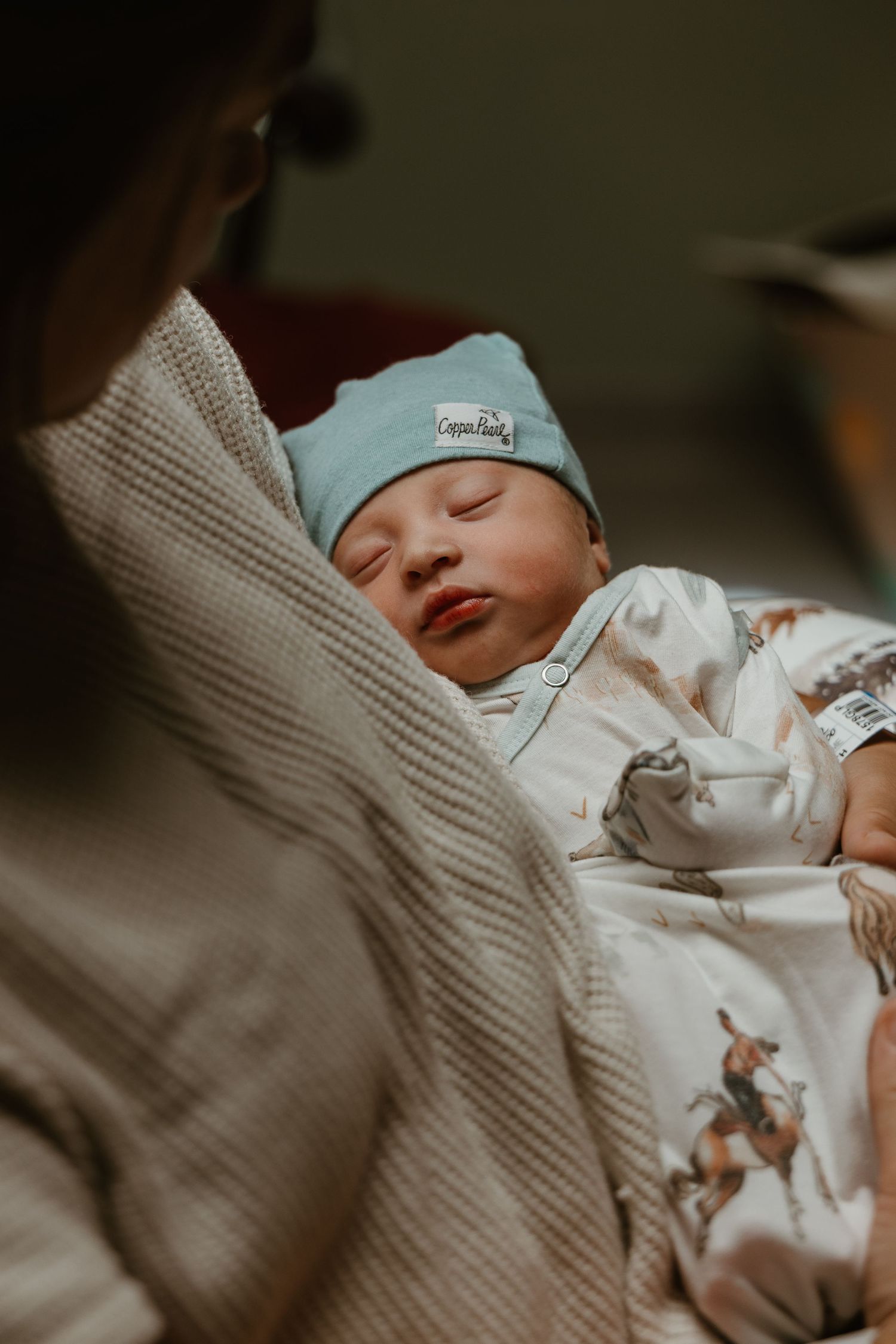 Newborn baby sleeping peacefully in white onesie with blue hat.