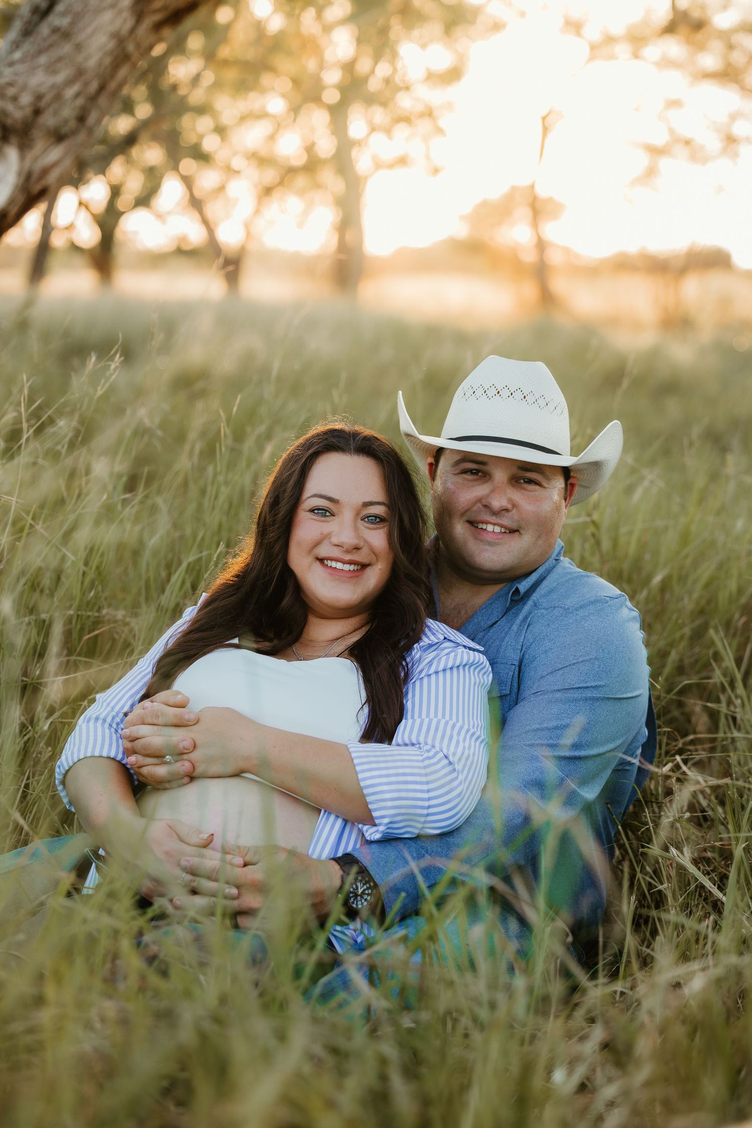 A couple embraces in tall grass during their sunset maternity photoshoot.