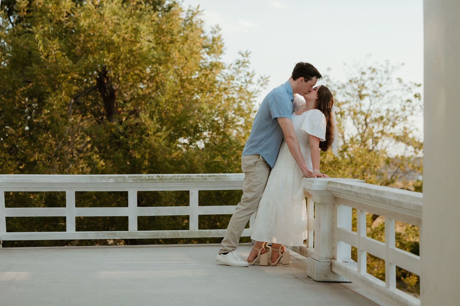 Engaged couple embracing each other on white balcony during golden hour at The Taylor Mansion in Taylor, TX.