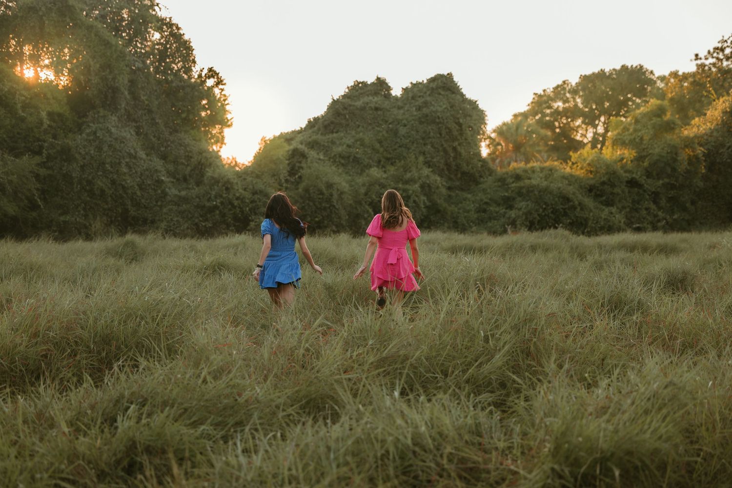 Two besties in bright dresses stand against a sunset-lit field of tall grass.
