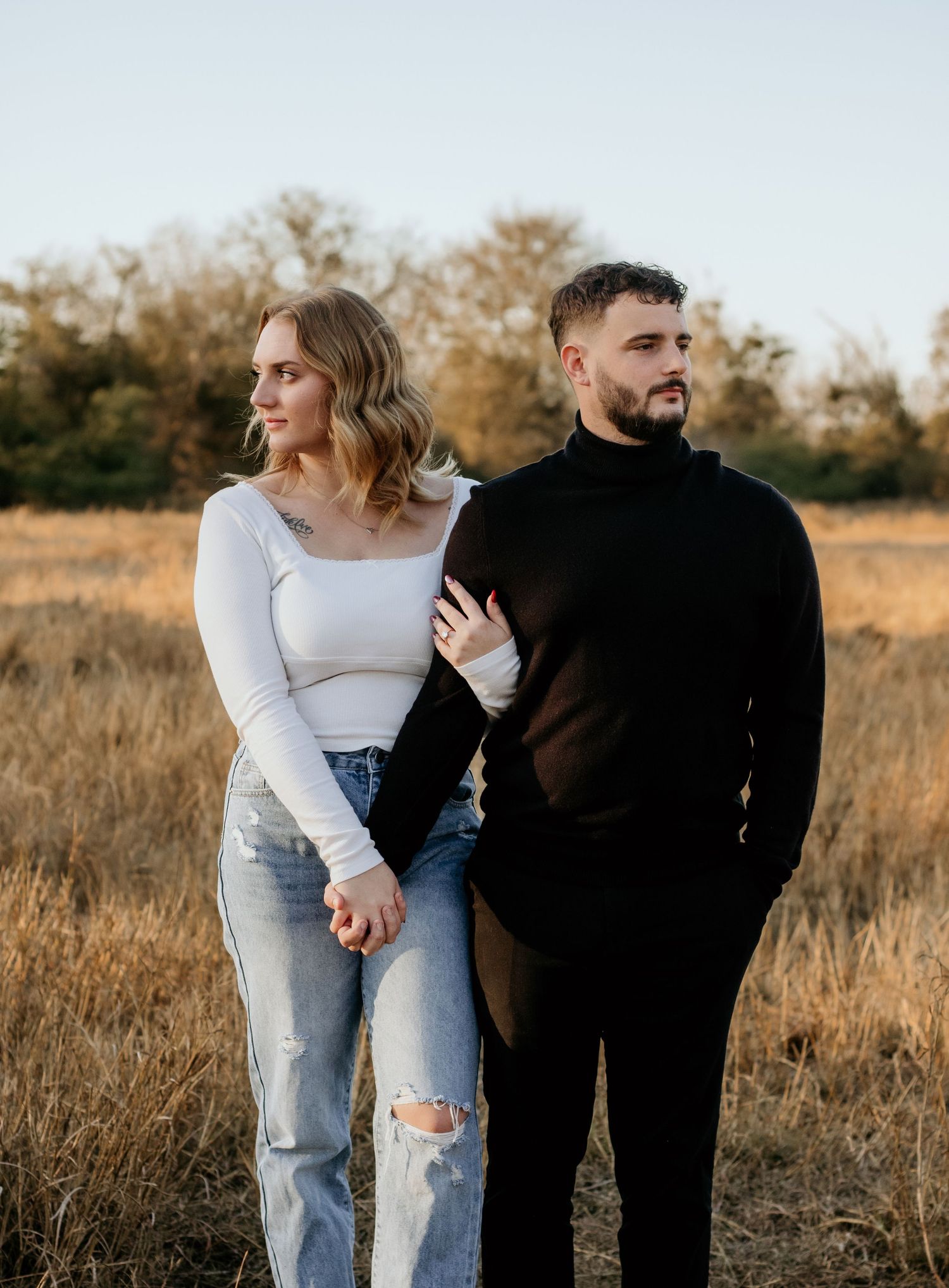 Engaged Couple in modern attire walking together through a golden autumn field at sunset.