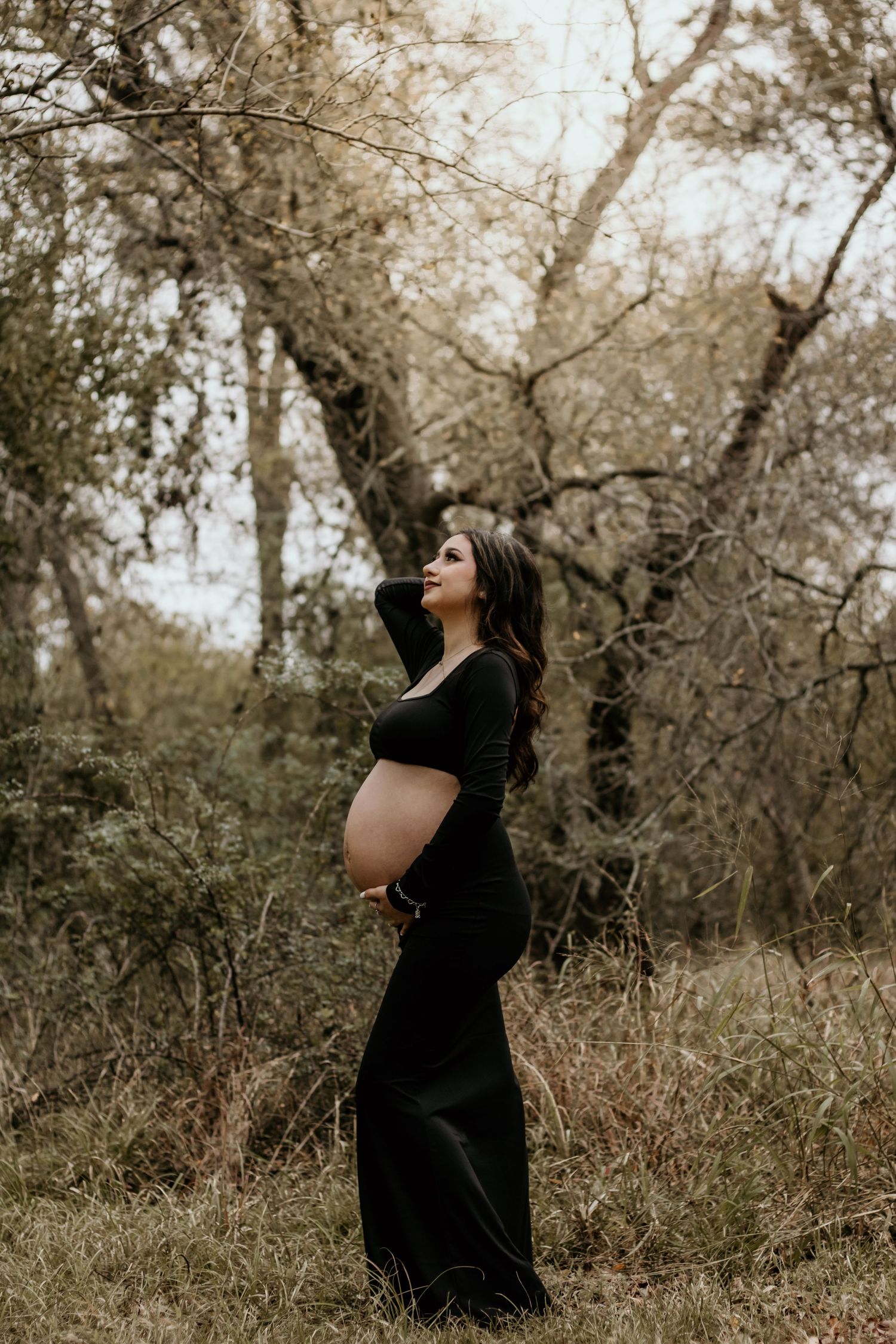 Artistic maternity photoshoot at golden hour with black dress and belly showing.