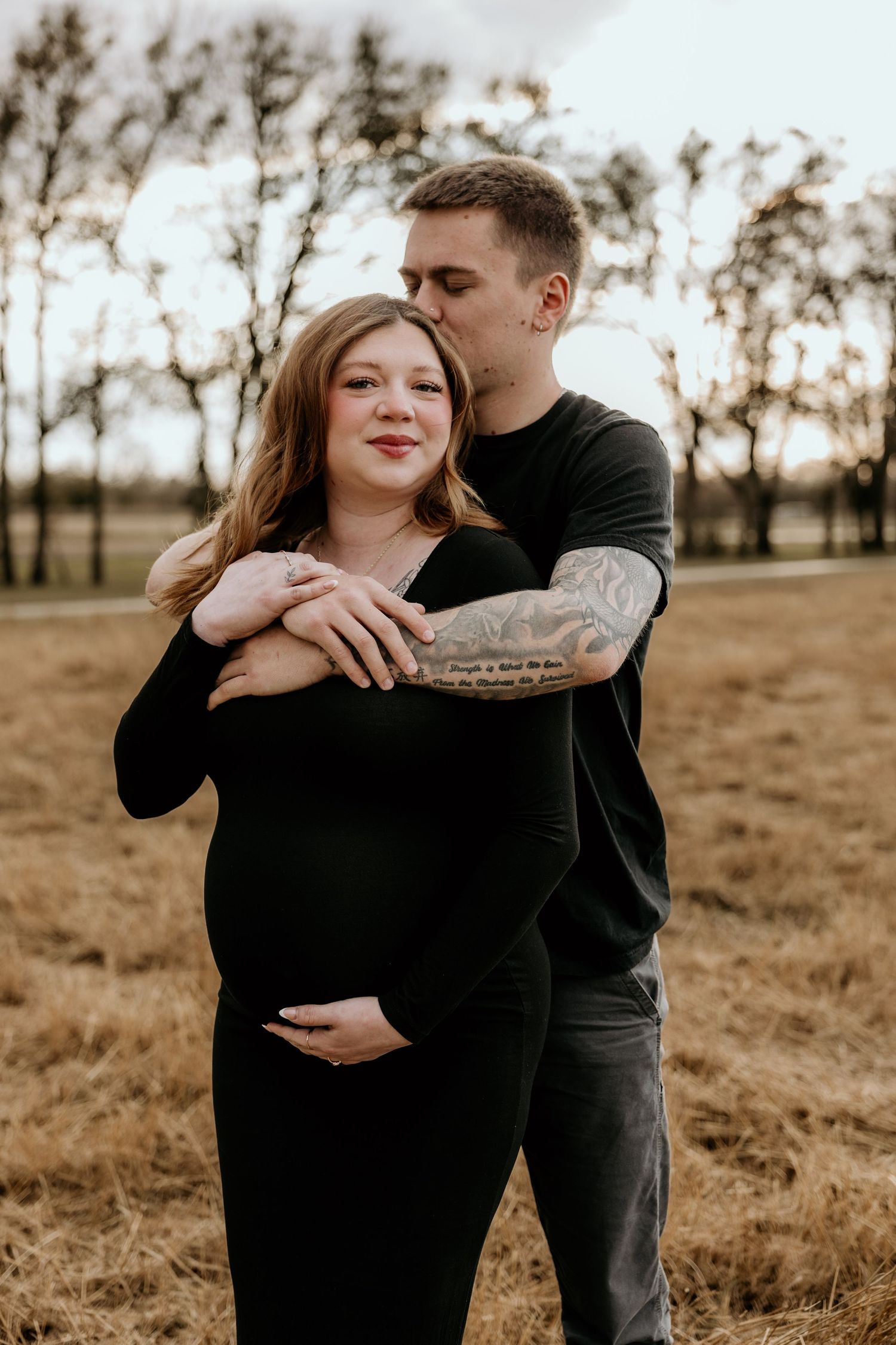 A couple embraces in a rustic outdoor setting during golden hour maternity photoshoot.