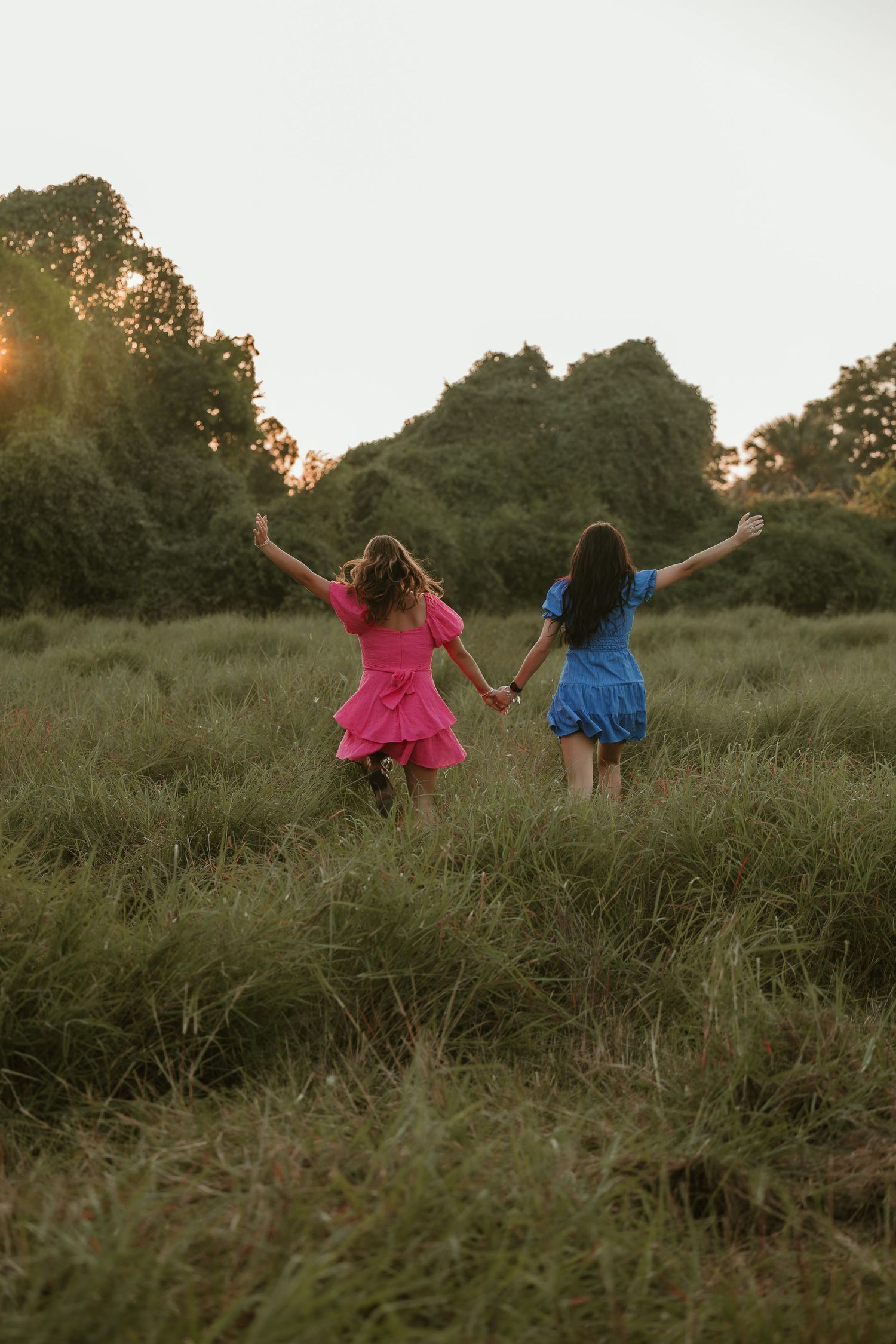 Friends hold hands while running through a wild meadow at sunset.