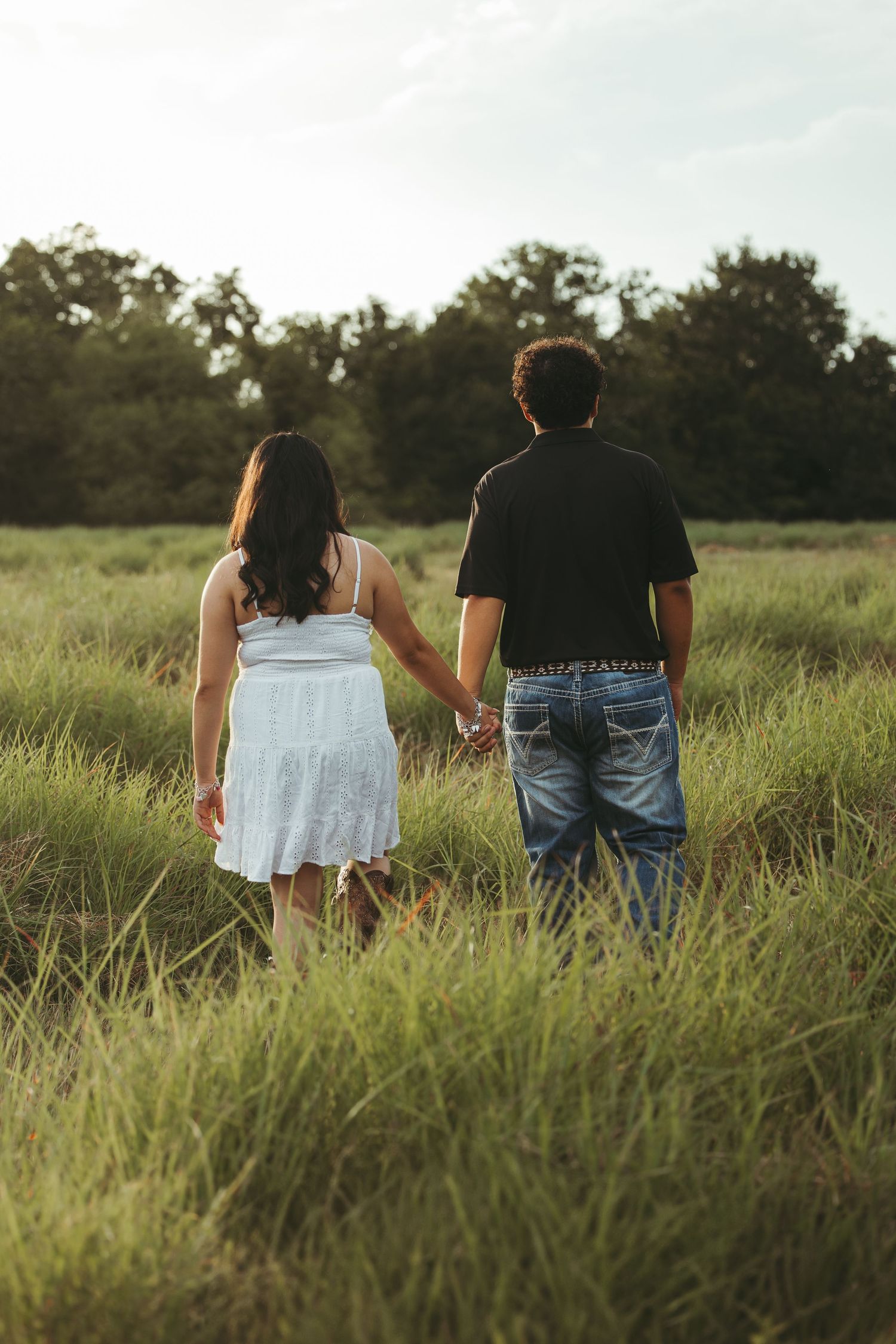 A couple walking through tall grass in a field during golden hour.