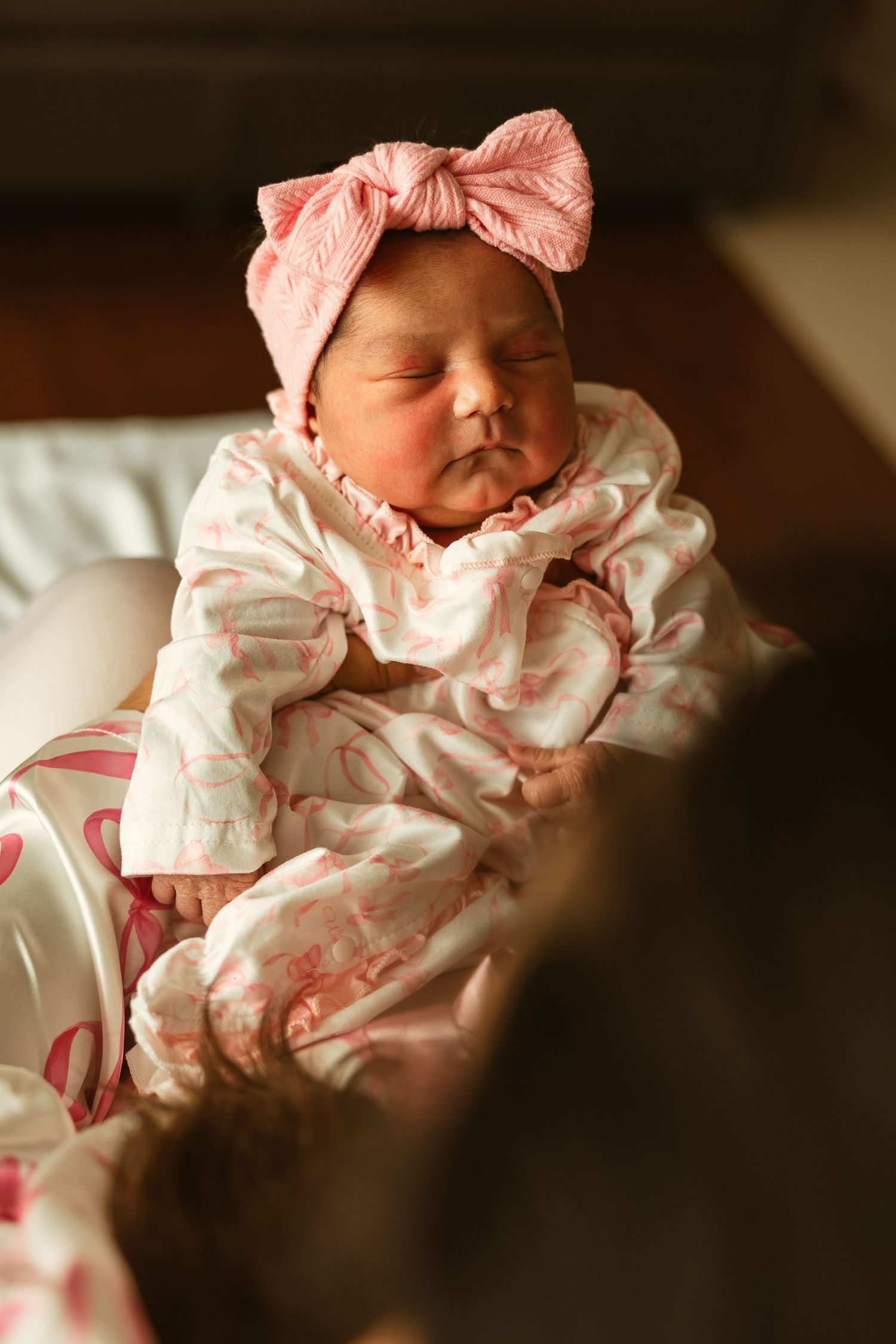 Newborn baby girl sleeping peacefully in pink floral outfit with matching pink bow headband.