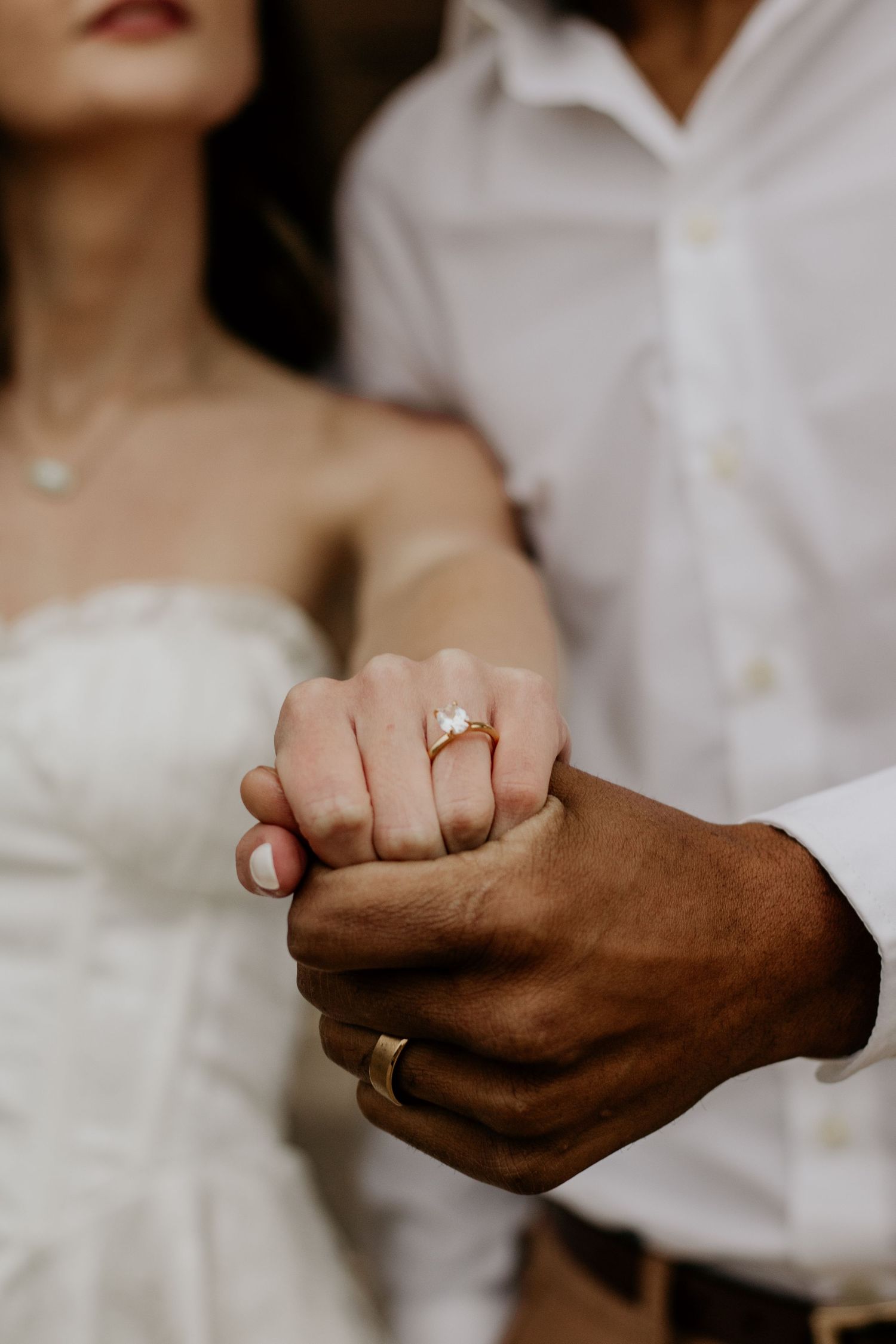 Close-up of hands holding each other with engagement ring in focus.