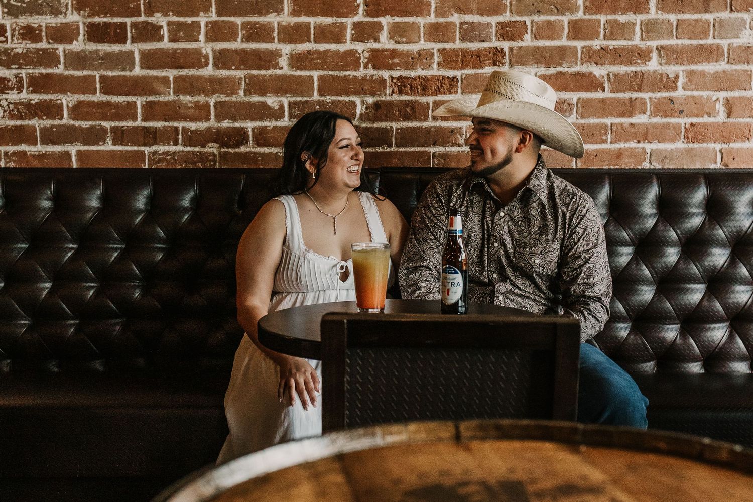 A romantic scene in a bar with exposed brick walls and leather booth seating.