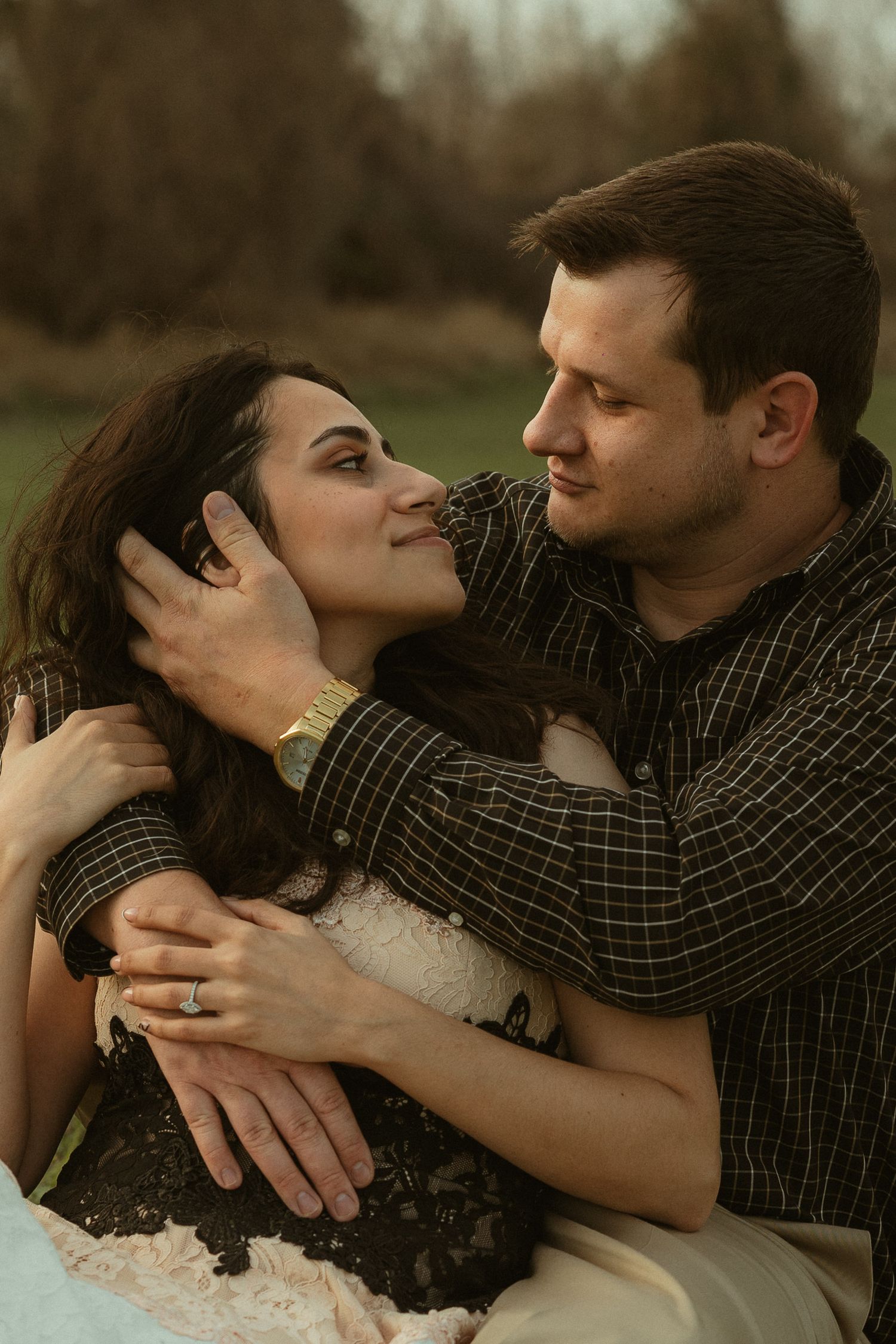 A couple shares a tender moment outdoors, man gently holding womans face as she gazes up at him lovingly.