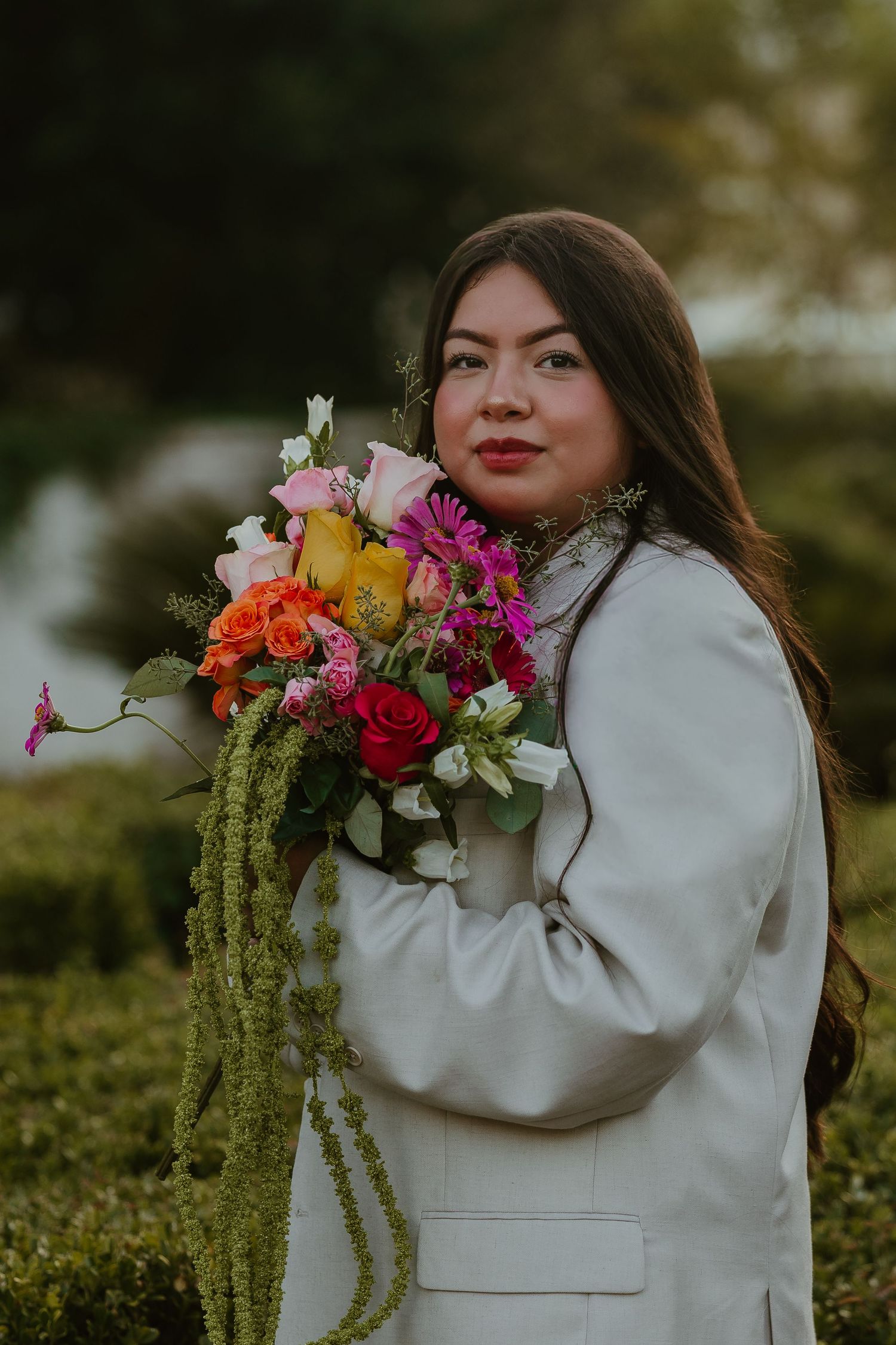 Person in white blazer holding vibrant floral bouquet with cascading amaranthus.