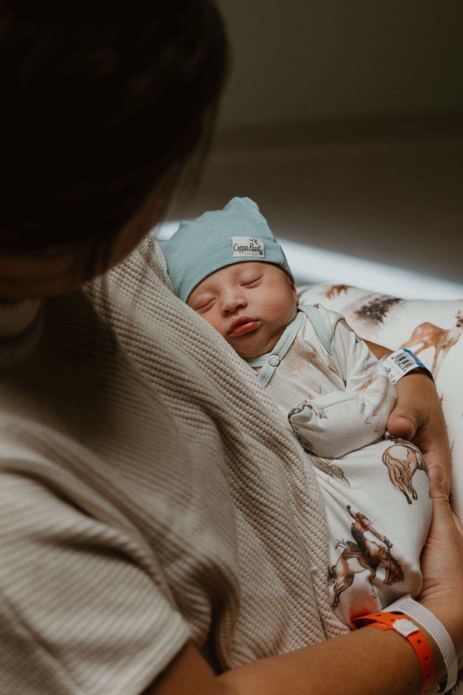 A sleeping newborn baby wrapped in a cozy knit blanket with animal print clothing.