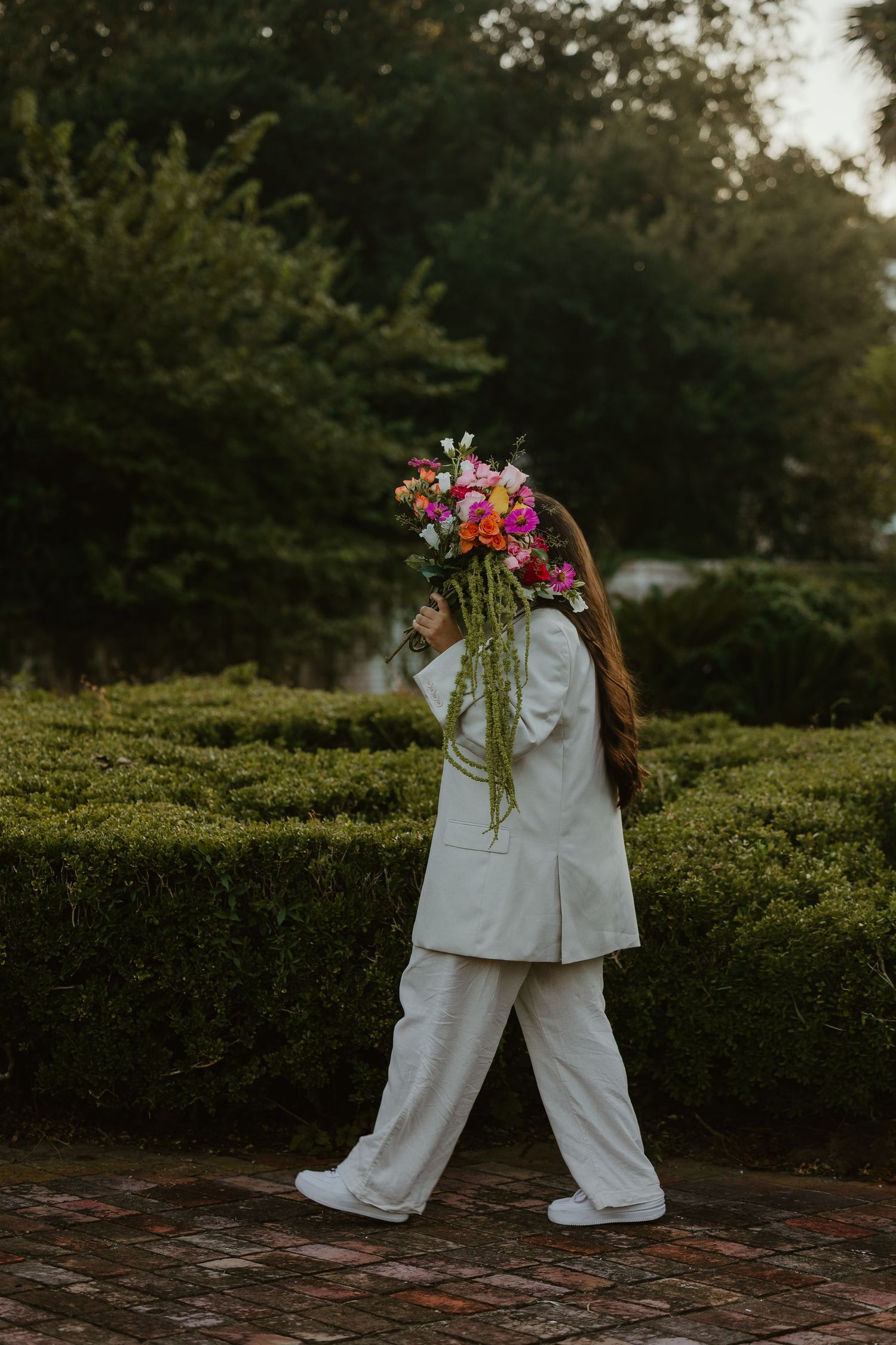 Candid shots of someone in white suit holding flowers while walking through a garden path.