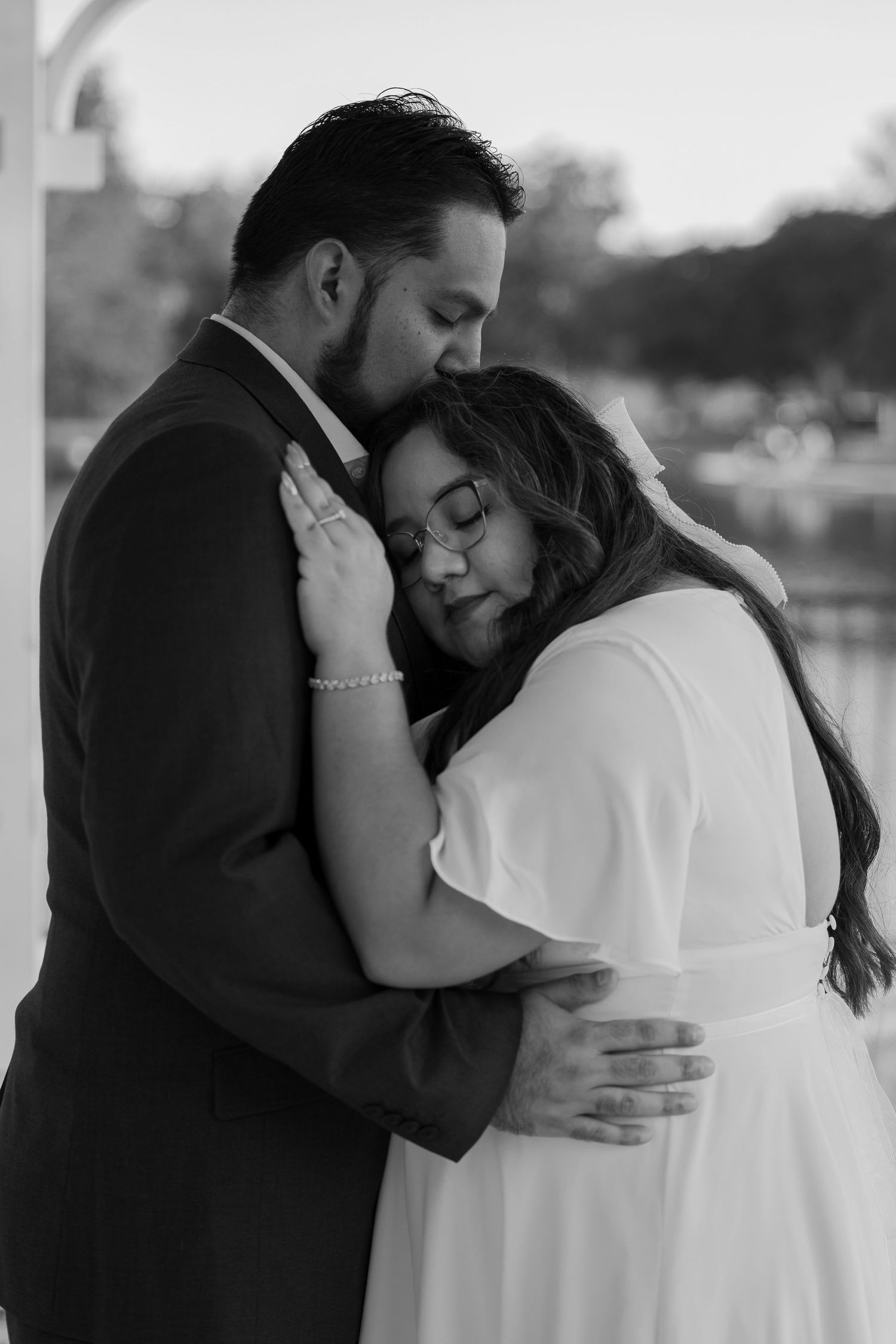 Intimate black and white portrait of couple in formal attire sharing tender embrace.