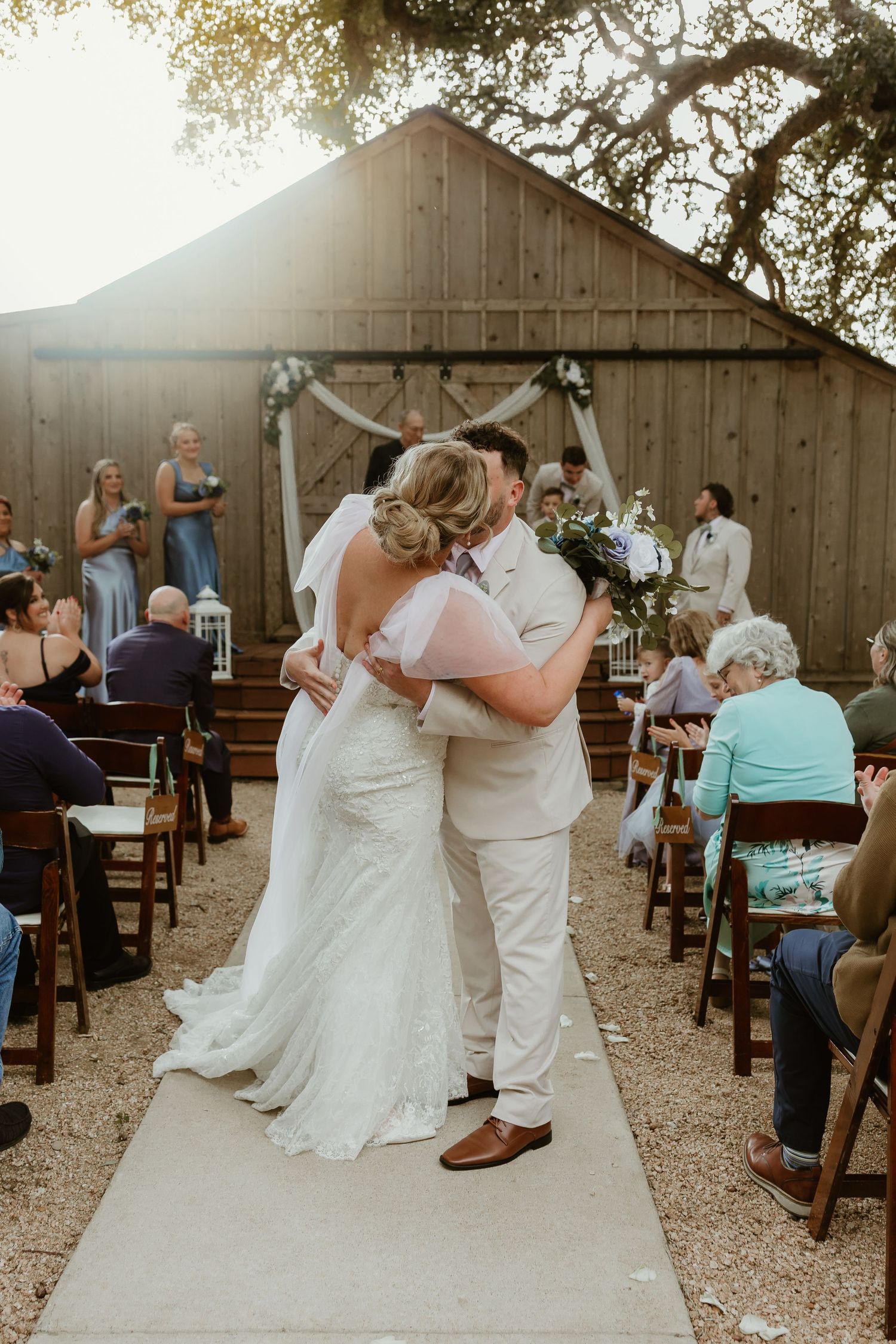 Rustic outdoor wedding ceremony with wooden chairs and natural tree backdrop.
