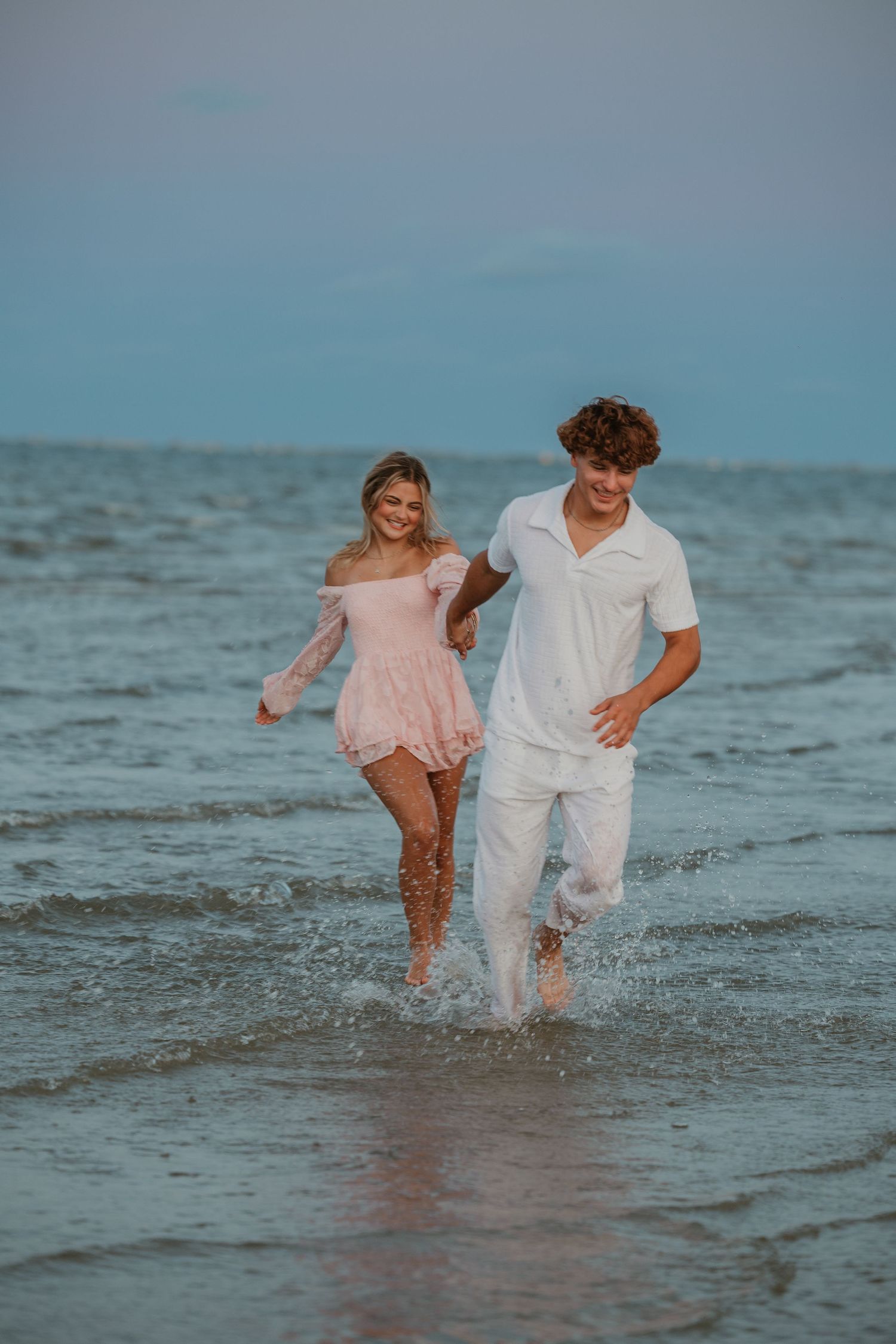A playful couple splashing in the shallow ocean water during sunset.